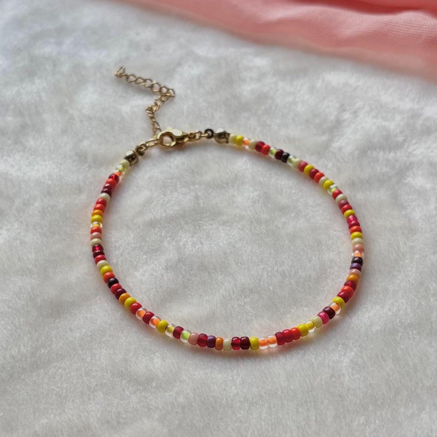 Multicolored beaded bracelet on a light gray surface with a pink fabric background