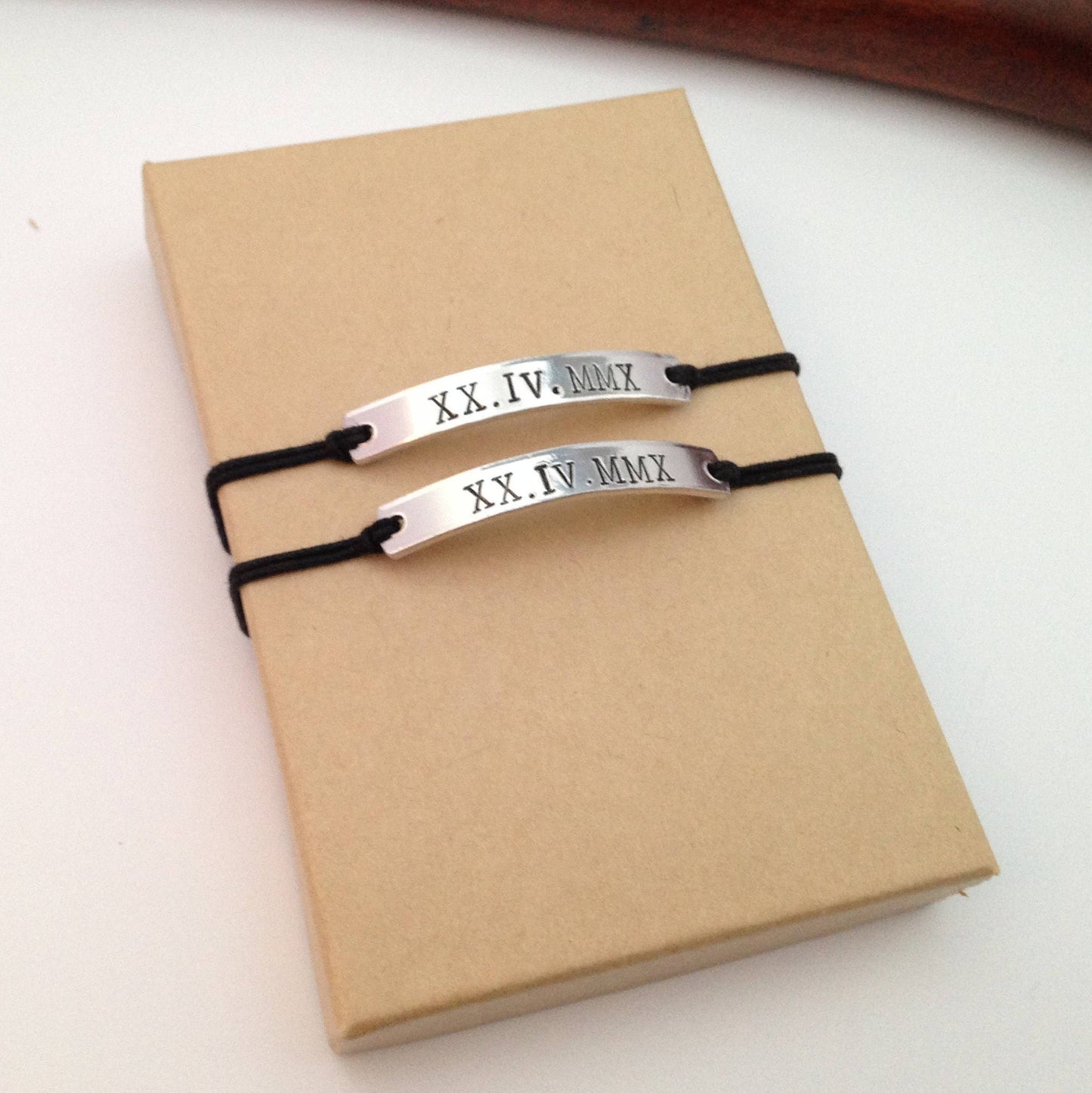 Two silver bracelets with Roman numeral markings on a brown box.