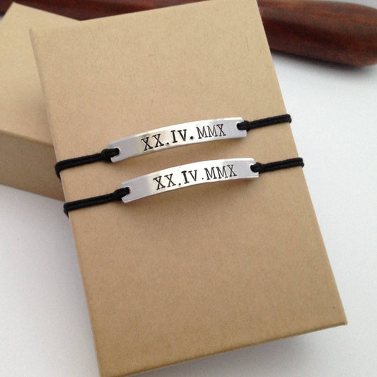 Two silver bracelets with Roman numeral markings on a brown box.