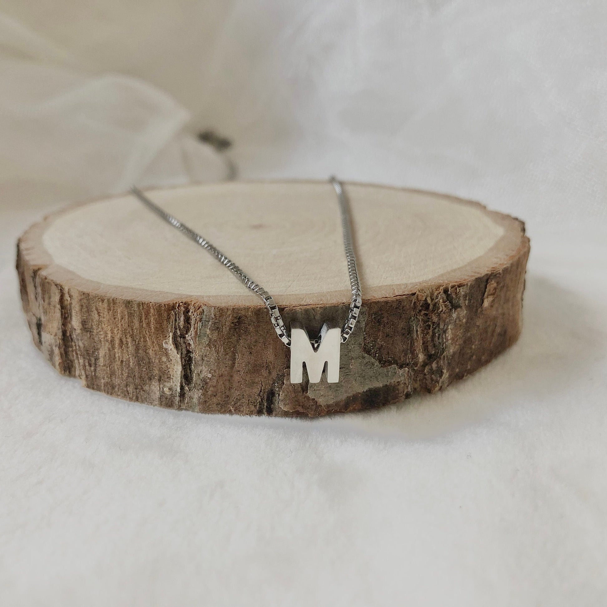 Silver necklace with a 'M' pendant on a wooden block