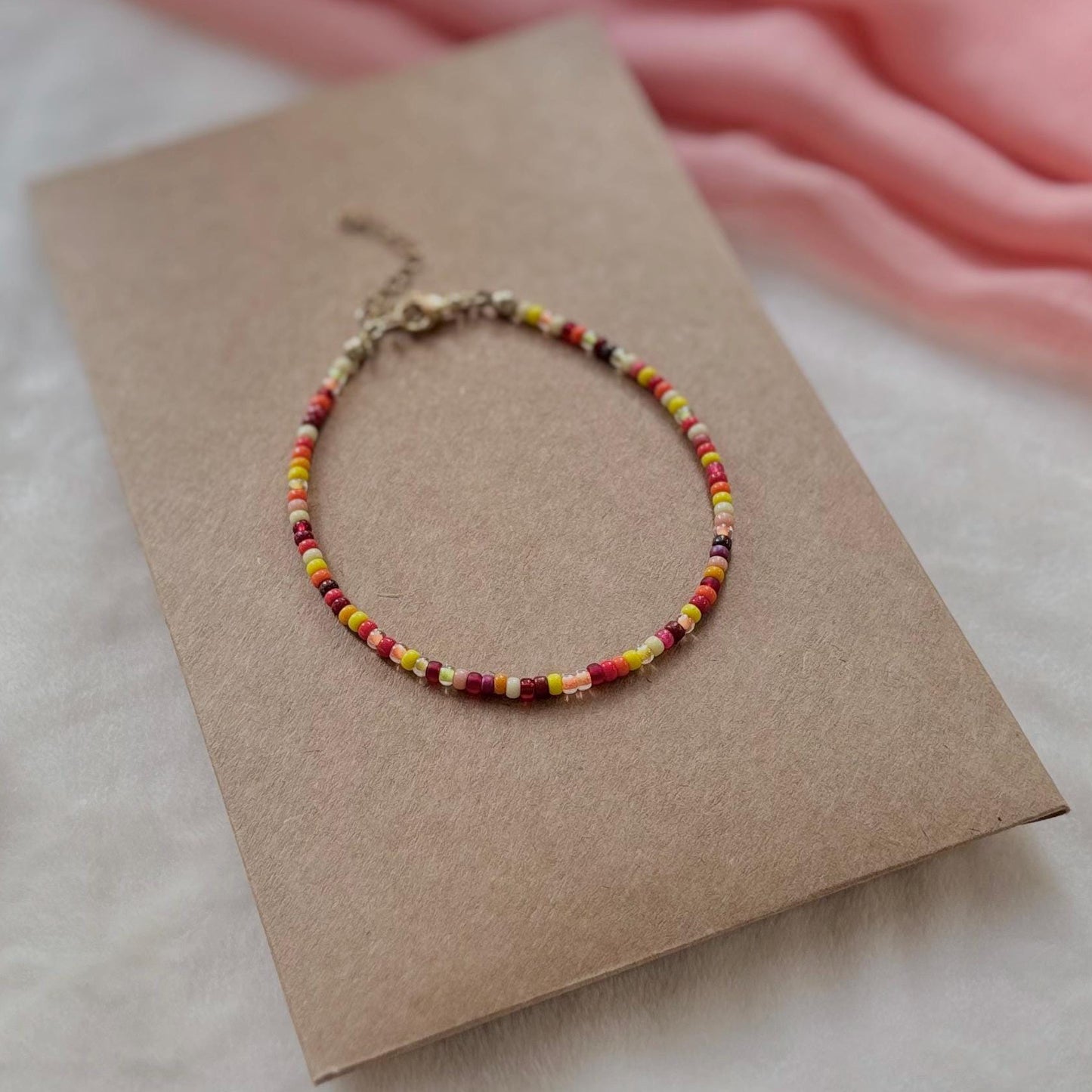 Multicolored beaded bracelet on a brown card with a pink fabric background