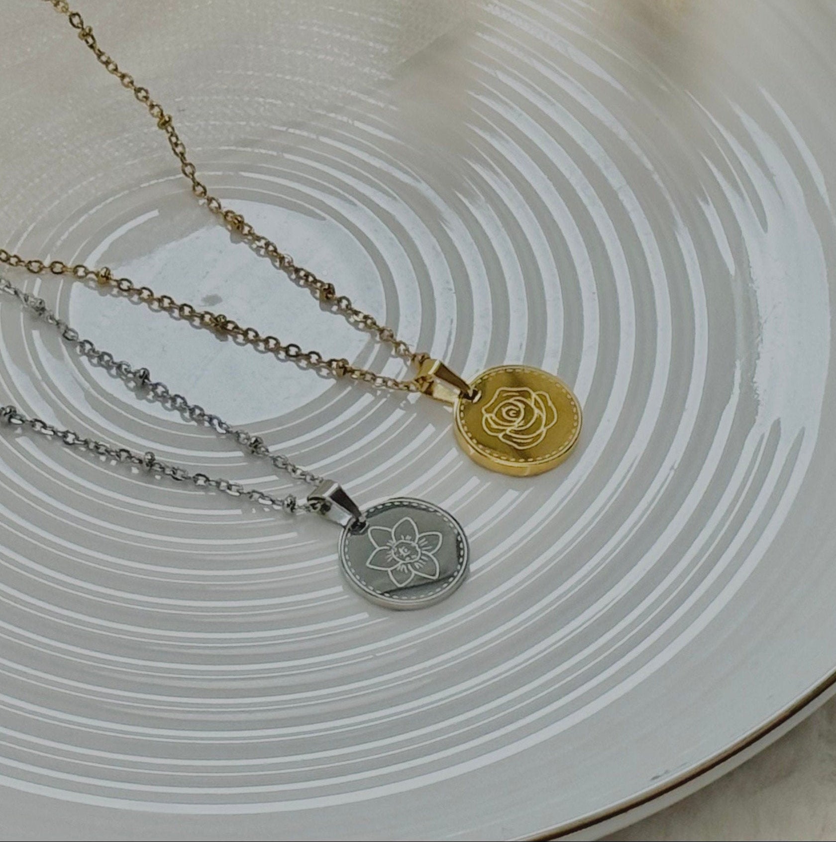 Two necklaces with pendants on a decorative plate with dried plants.