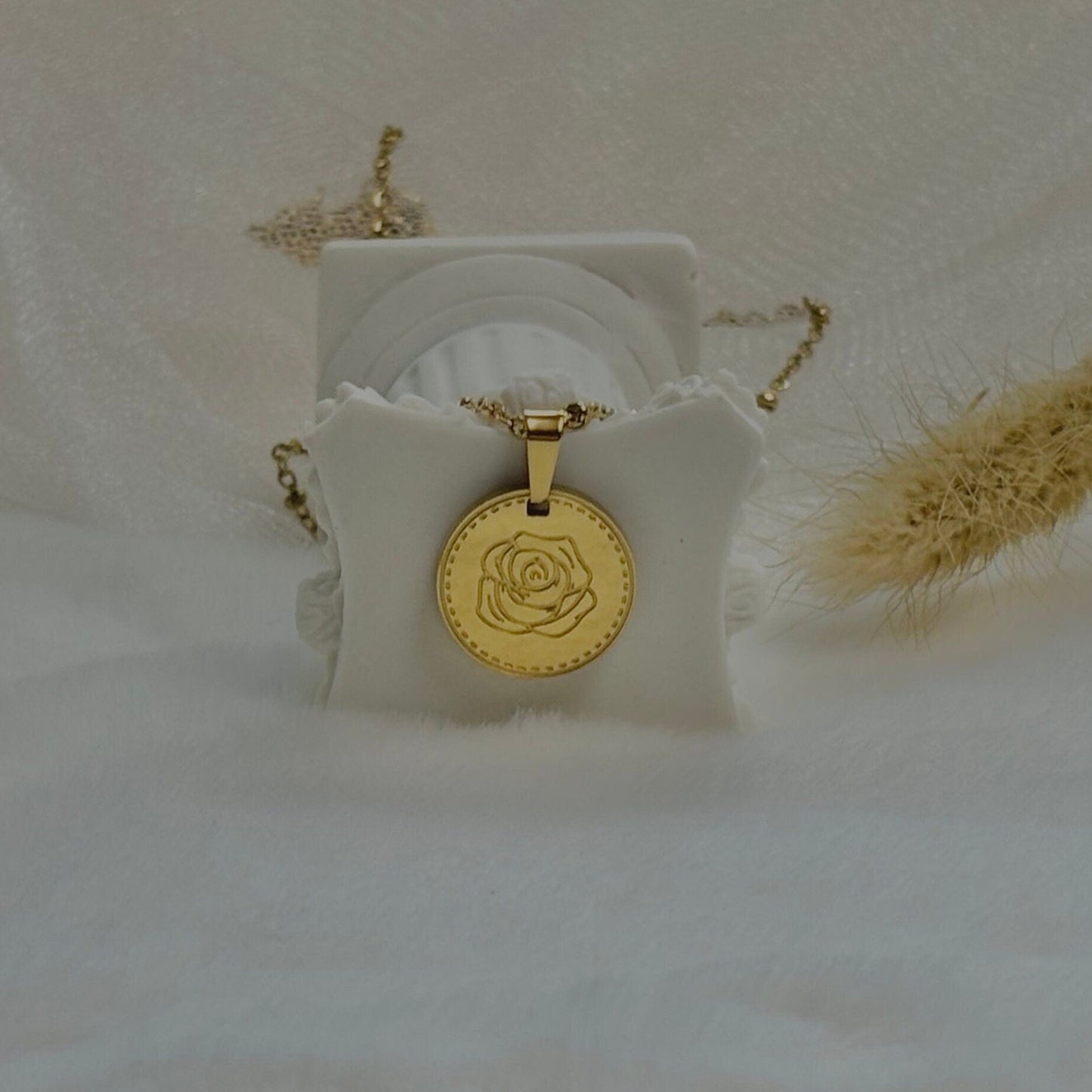 Gold necklace with a rose pendant on a white stand against a soft beige background