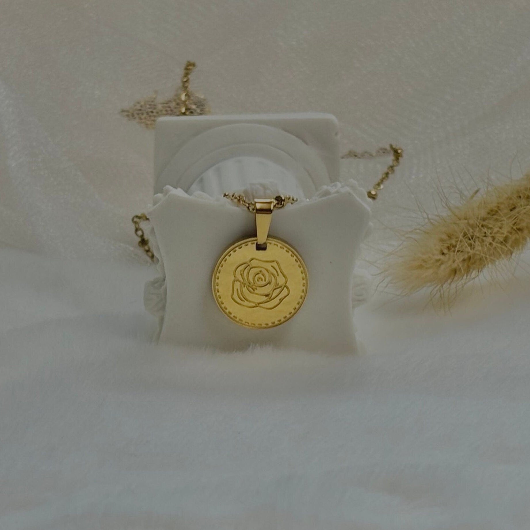 Gold necklace with a rose pendant on a white stand against a soft beige background