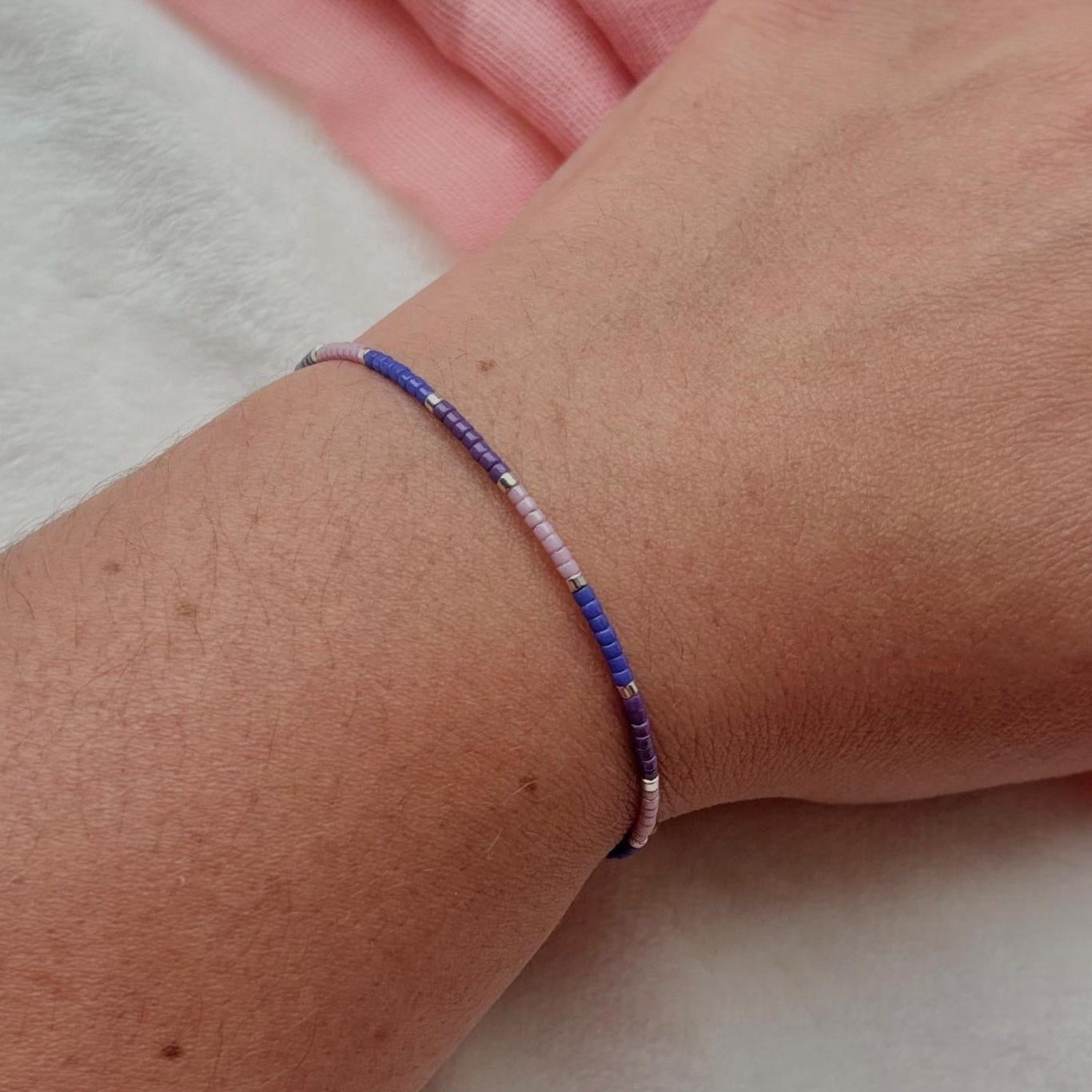 Close-up of a wrist wearing a blue beaded bracelet on a light background