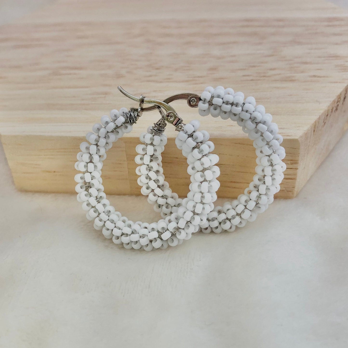 White beaded hoop earrings on a wooden block