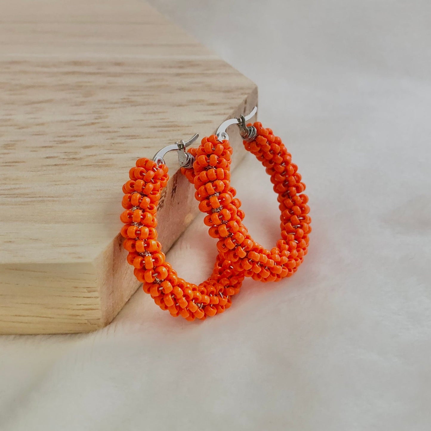 Orange beaded hoop earrings on a wooden block with a white background