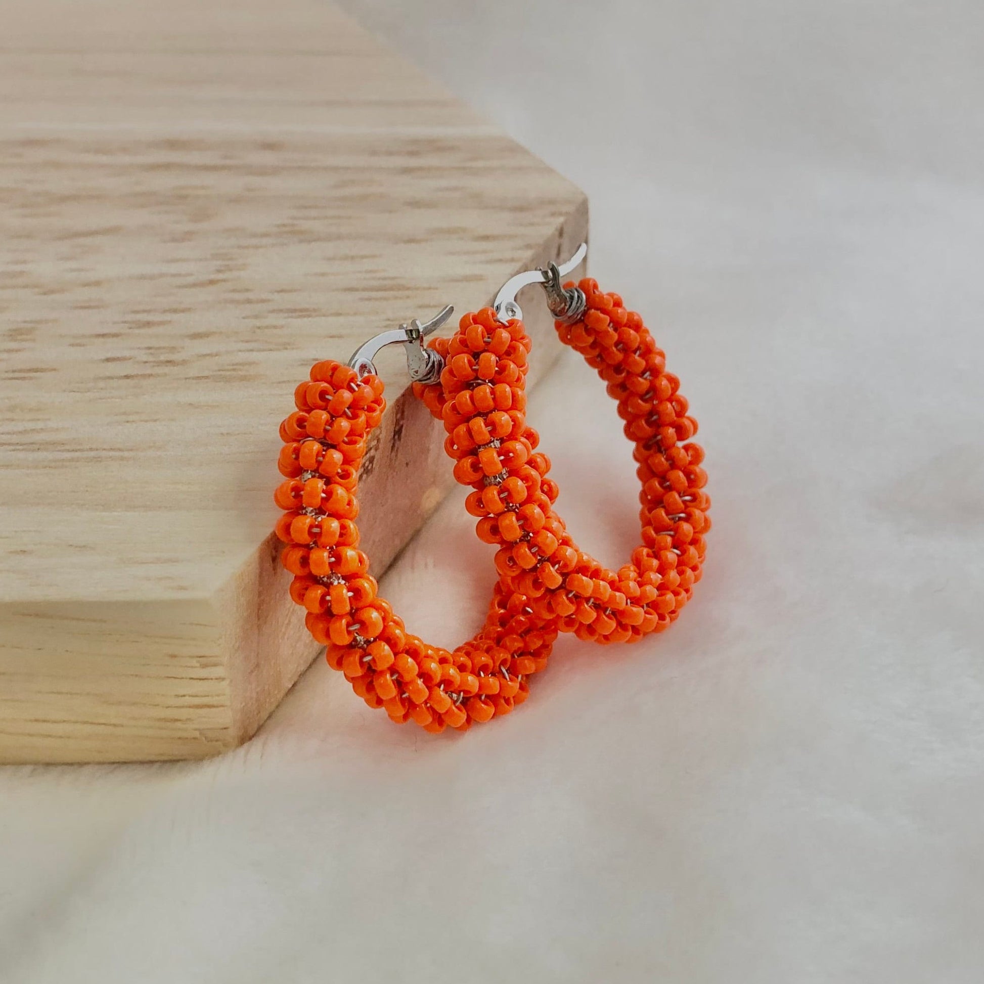 Orange beaded hoop earrings on a wooden block with a white background