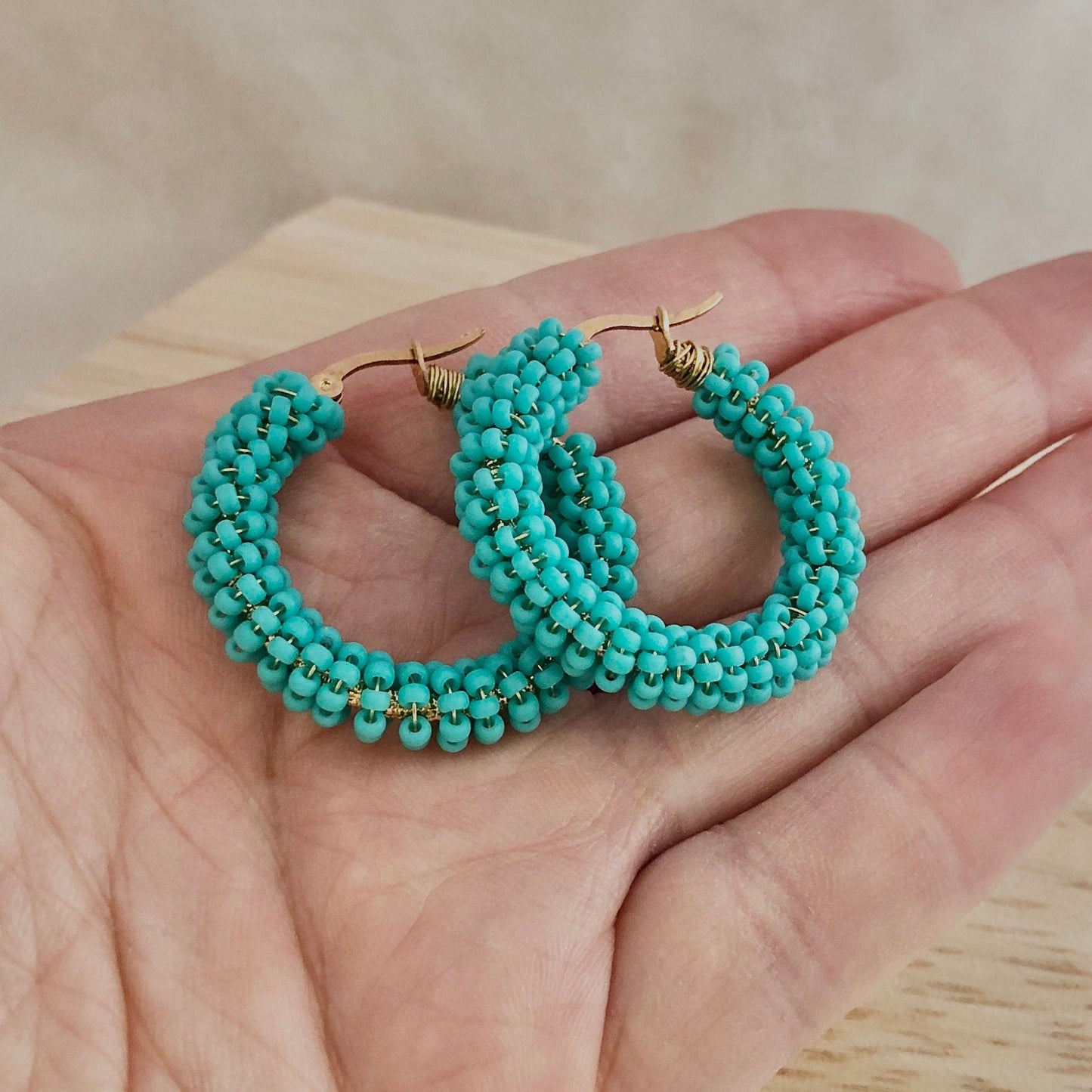 Turquoise beaded hoop earrings held in a hand with a neutral background