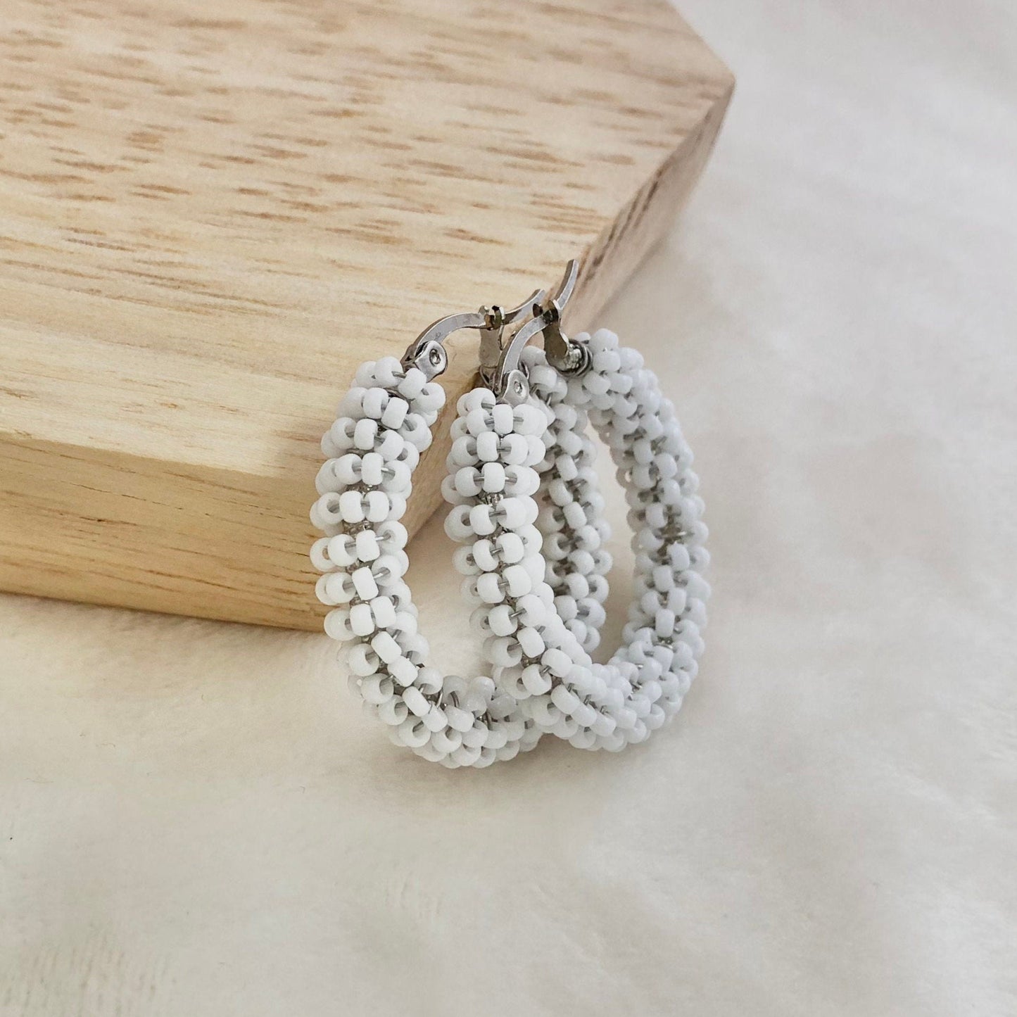 White beaded hoop earrings on a wooden block with a neutral background