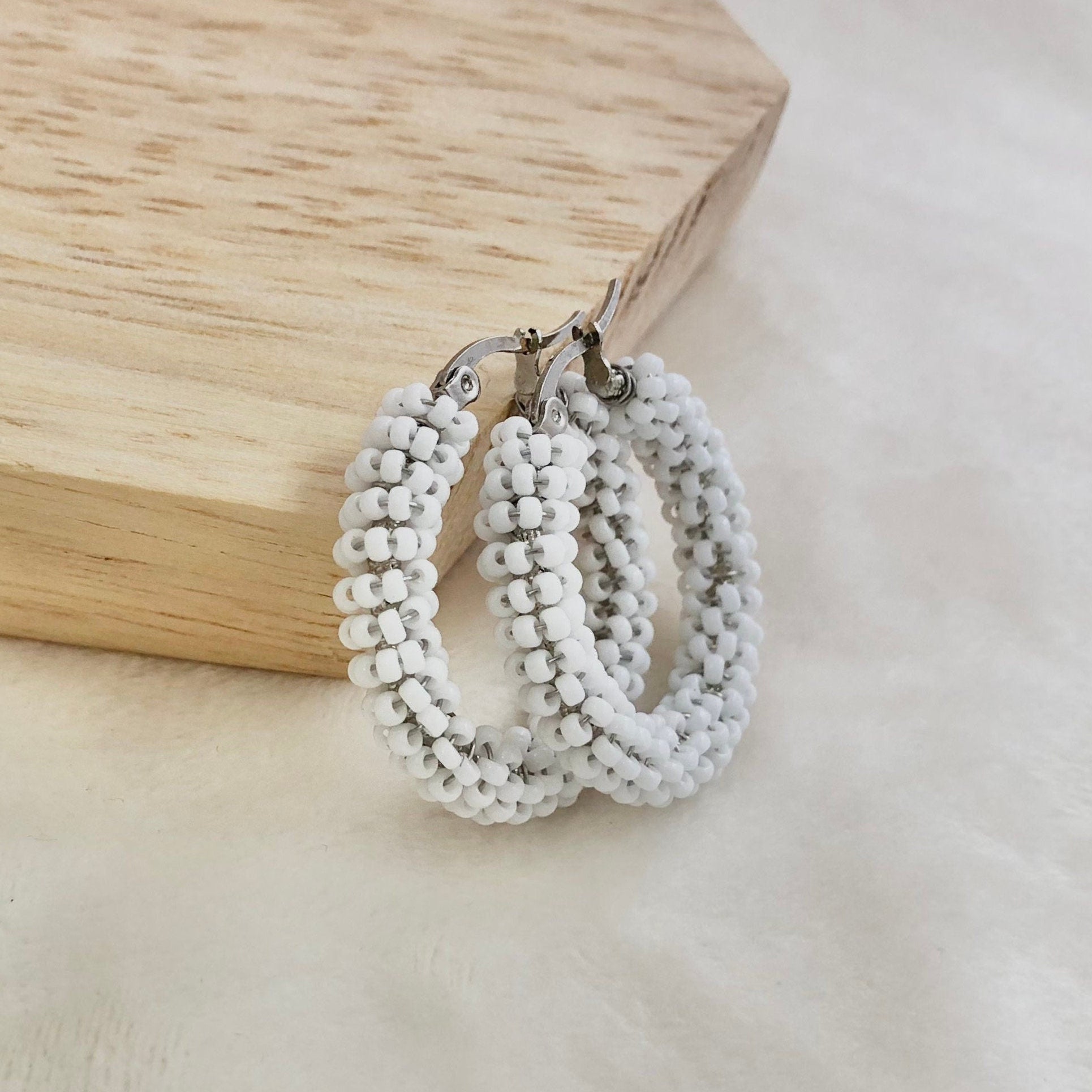 White beaded hoop earrings on a wooden block with a neutral background