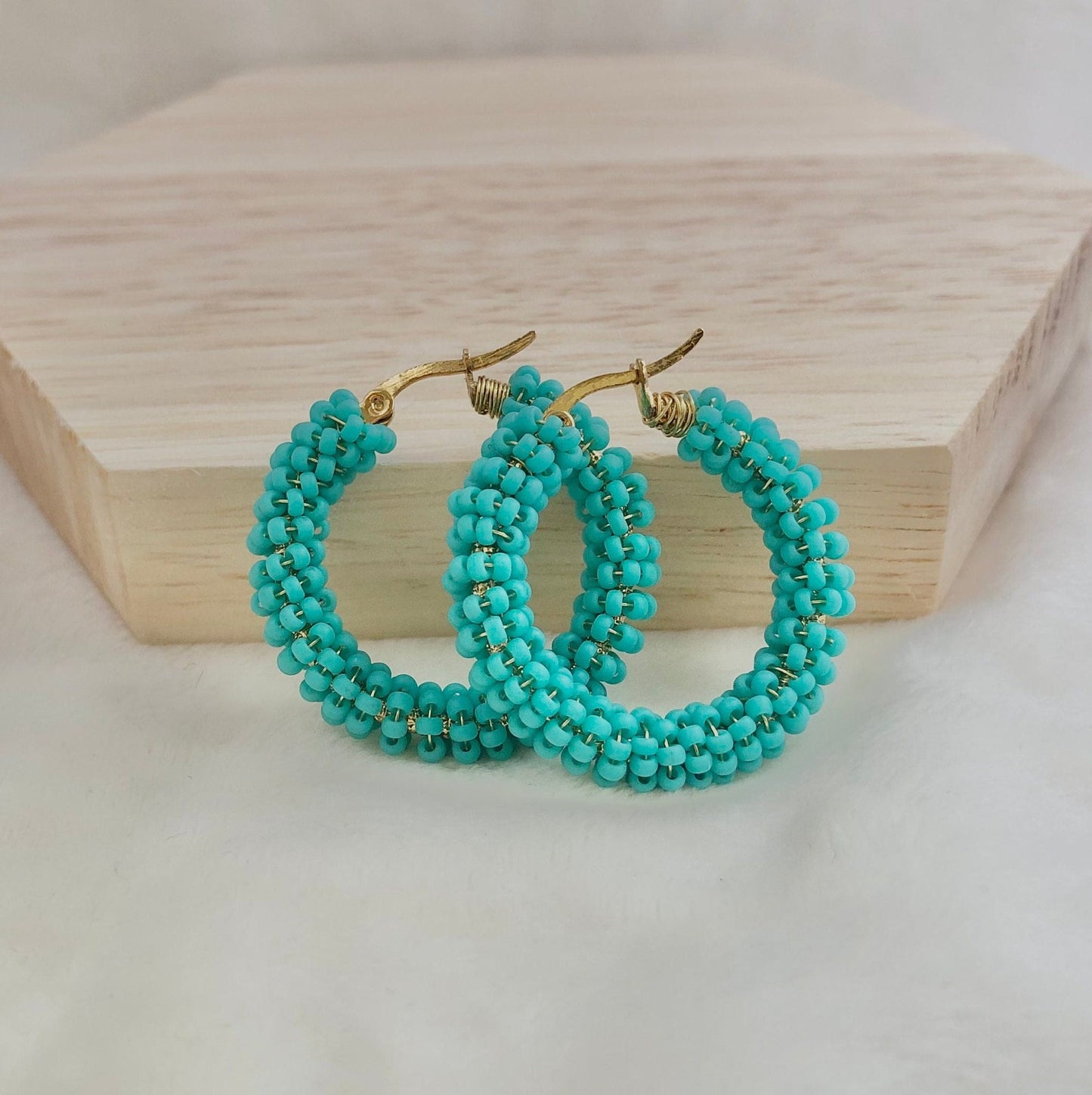 Turquoise beaded hoop earrings on a wooden block with a white background