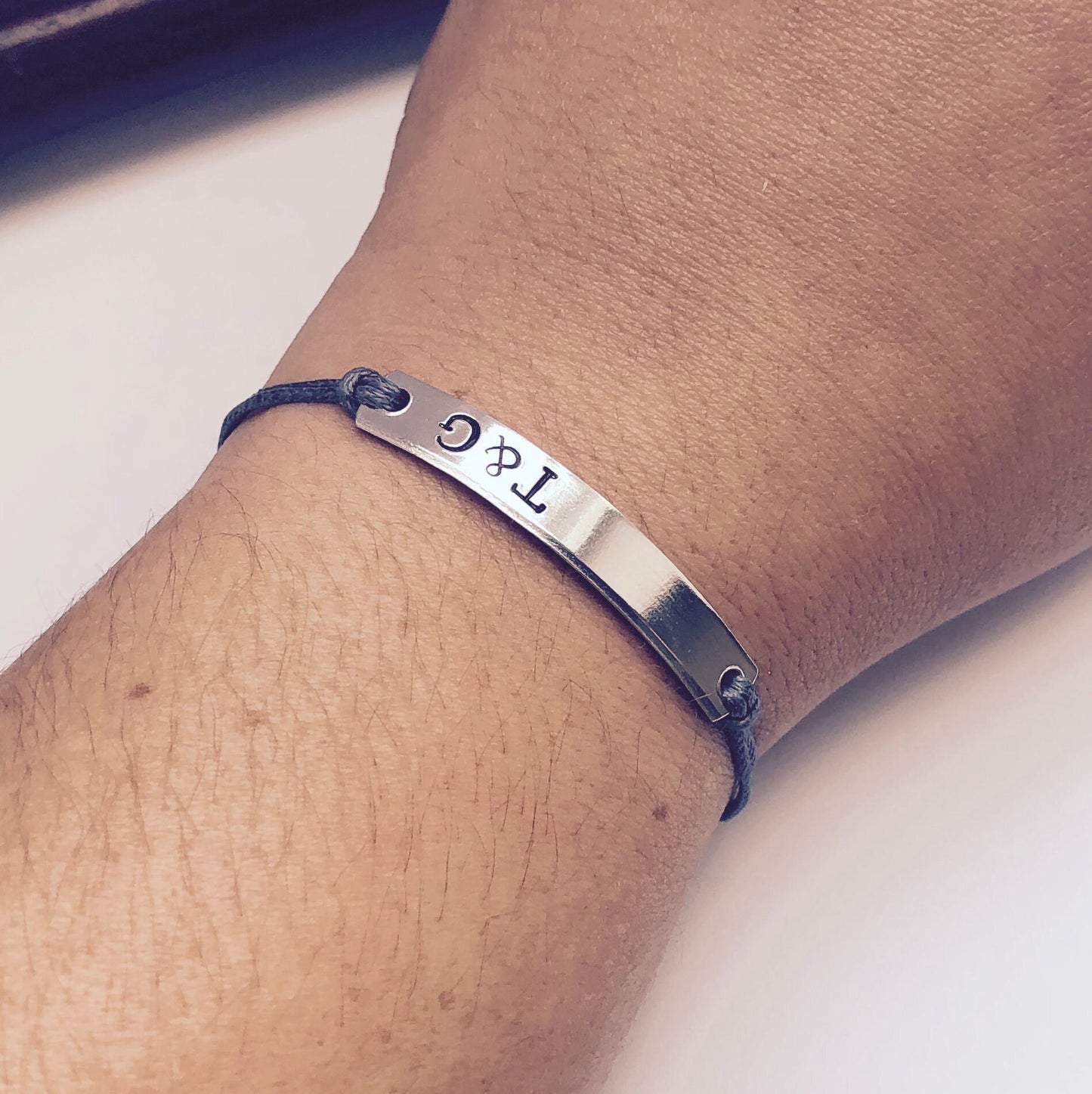 Silver bracelet with engraved text on a wrist against a neutral background