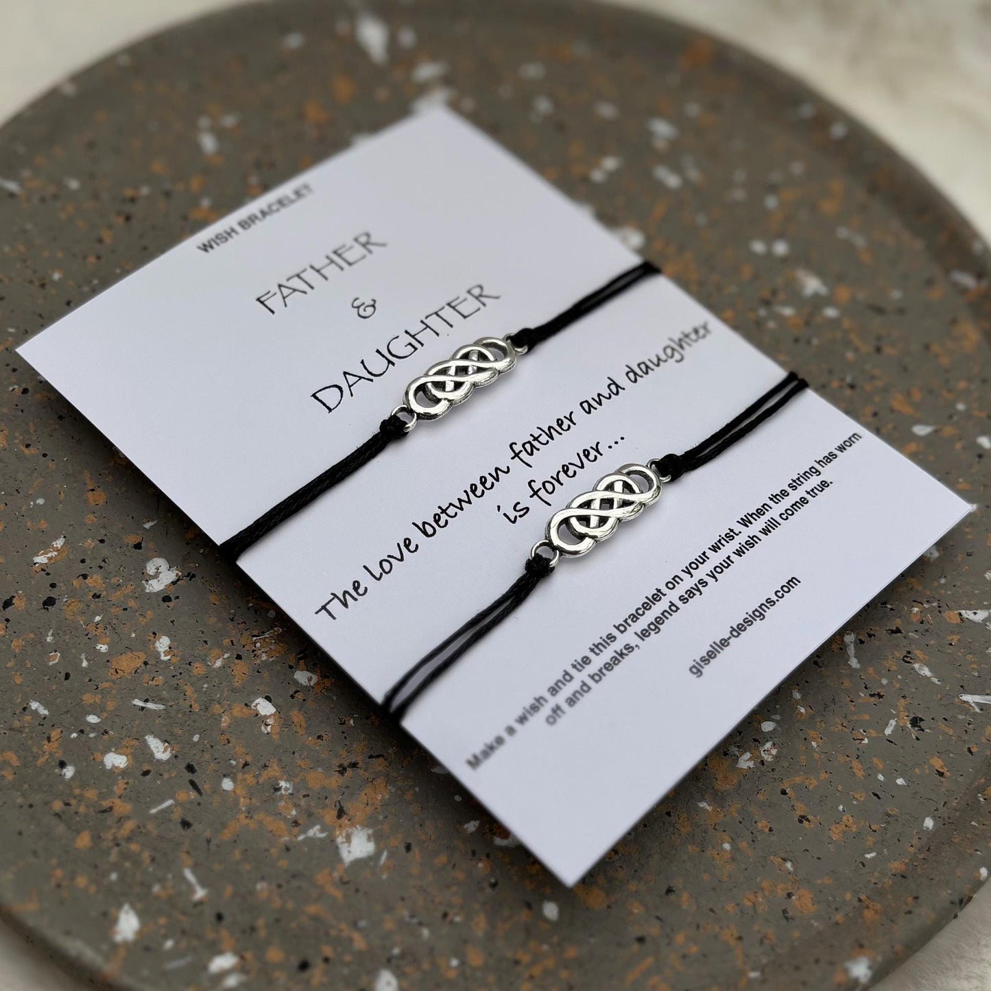 Two black braided bracelets on a white card with text on a speckled gray surface