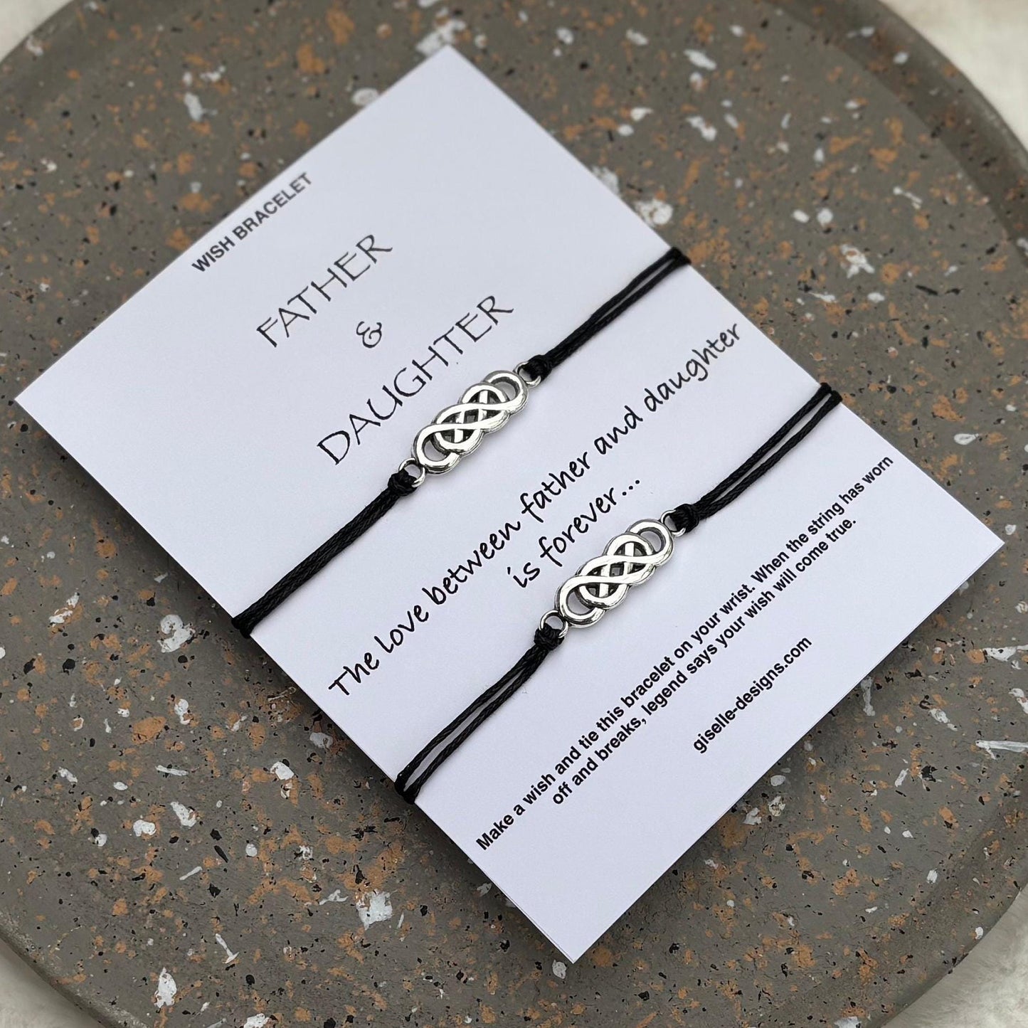 Two intertwined bracelets on a card with text on a speckled stone surface