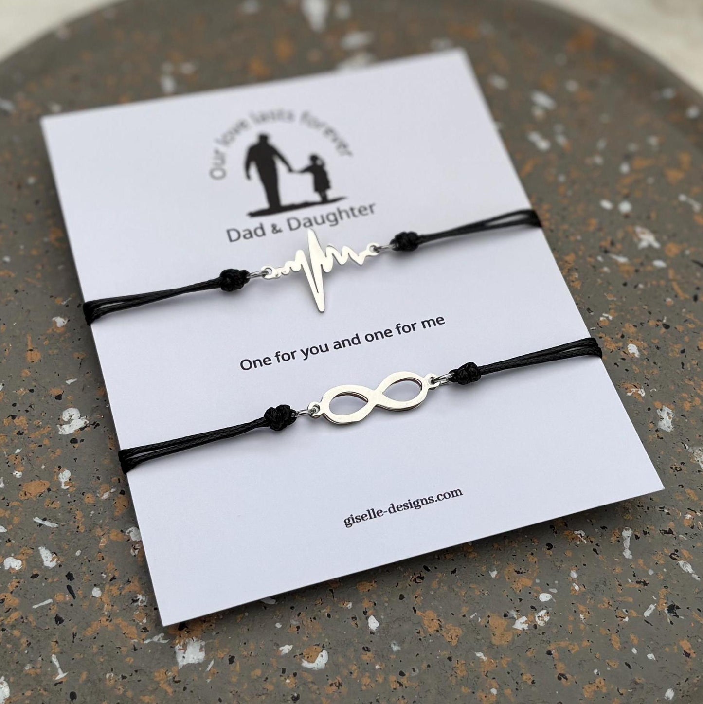 Two black bracelets with unique designs on a branded card, placed on a textured surface.