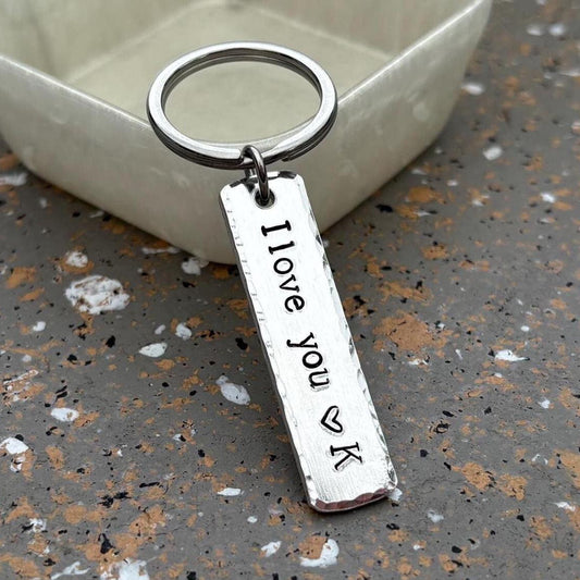 Silver keychain with 'I love you' tag on a textured surface