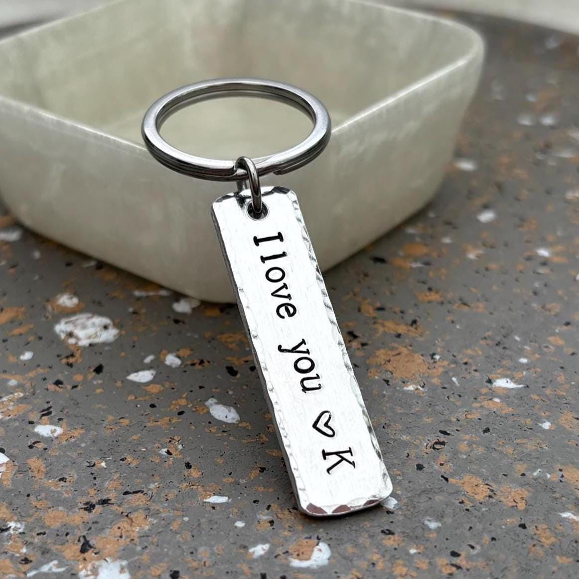 Silver keychain with 'I love you VK' engraving on a speckled surface