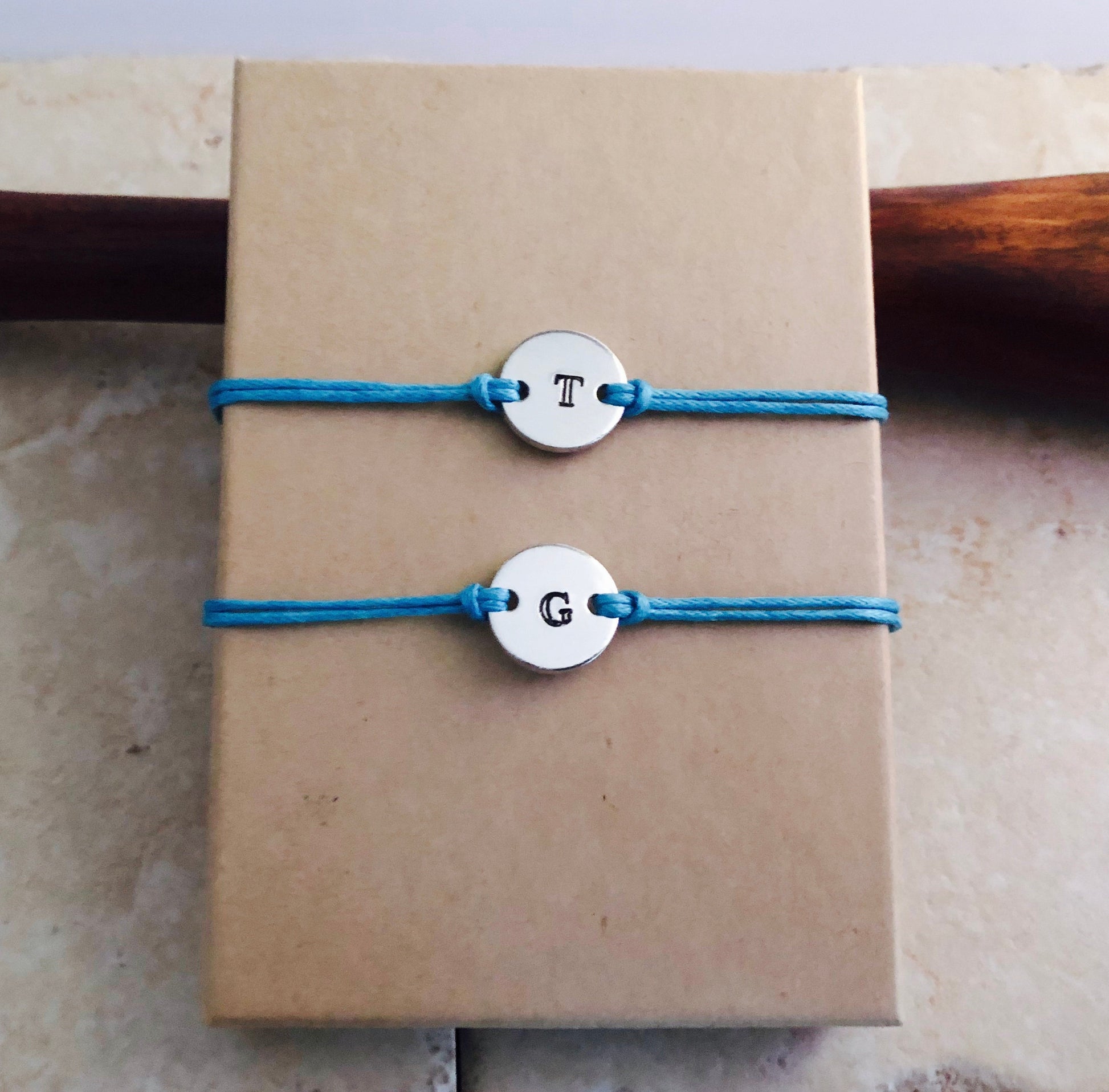Two blue bracelets with silver charms on a brown paper bag.