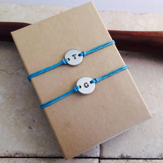 Two blue bracelets with letter charms on a brown box.