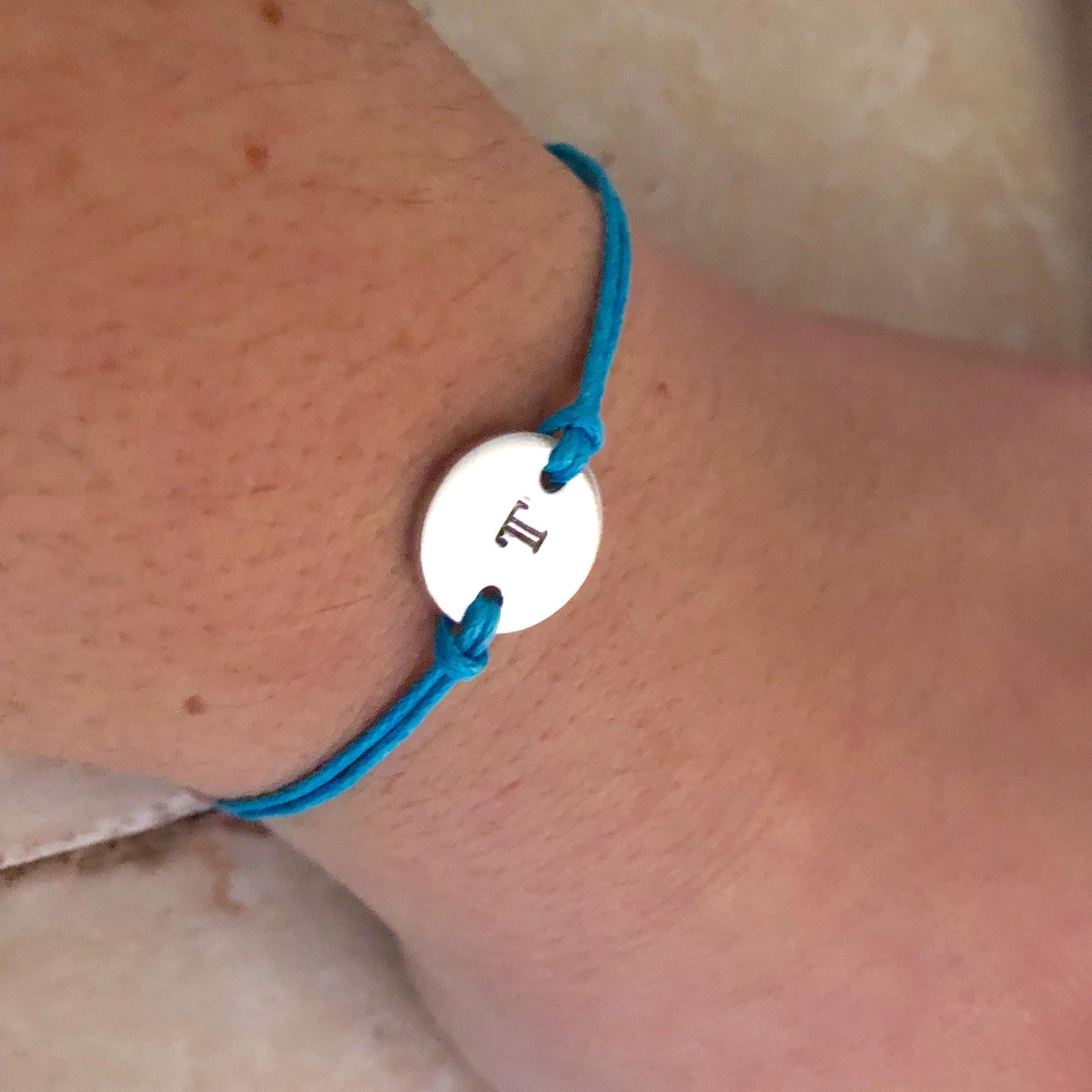 Blue bracelet with a silver disc featuring a letter 'T' on a wrist.
