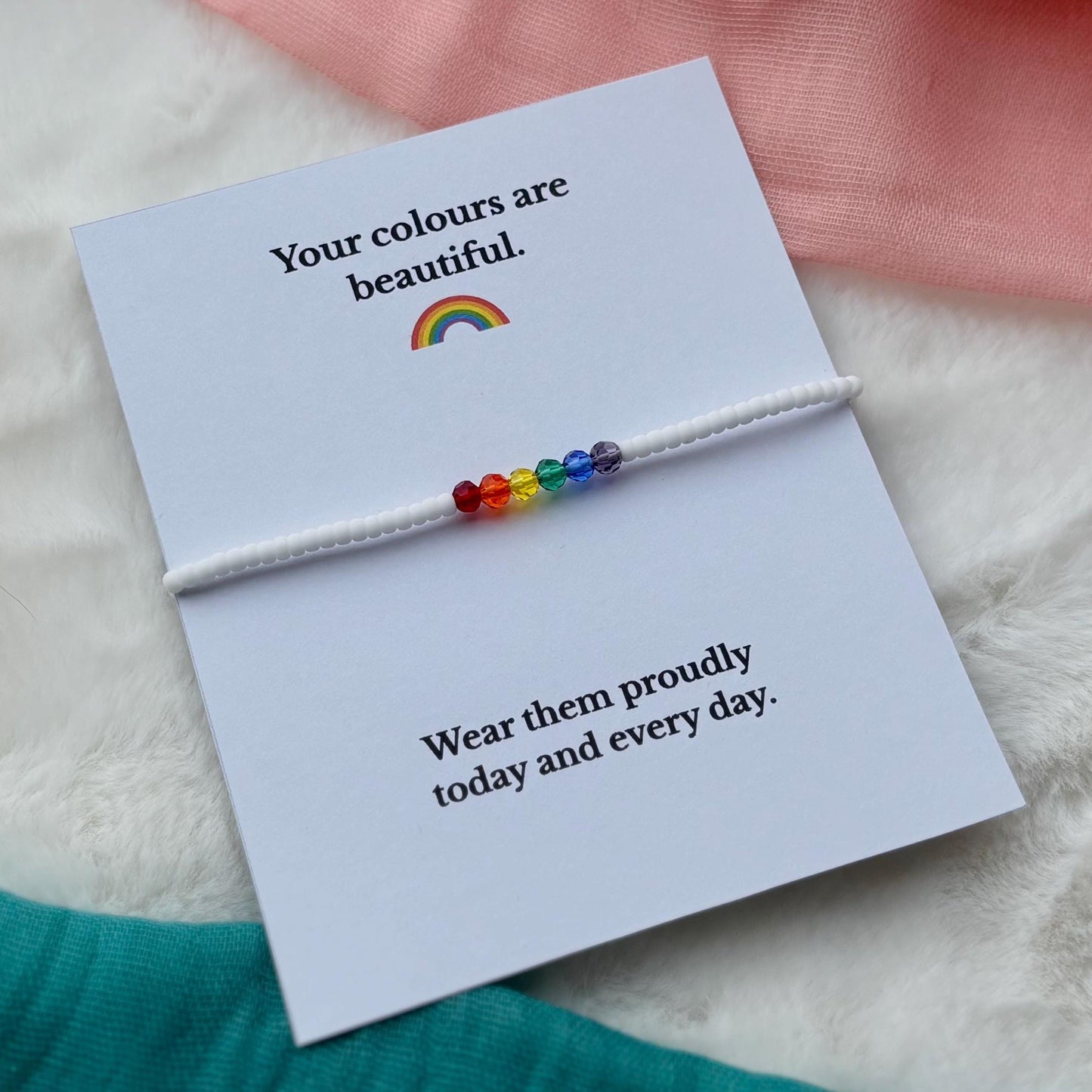 Rainbow bracelet on a card with text message, placed on a soft surface.