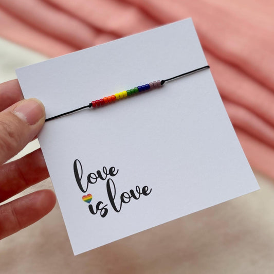 Hand holding a card with 'love is love' and a rainbow bracelet.