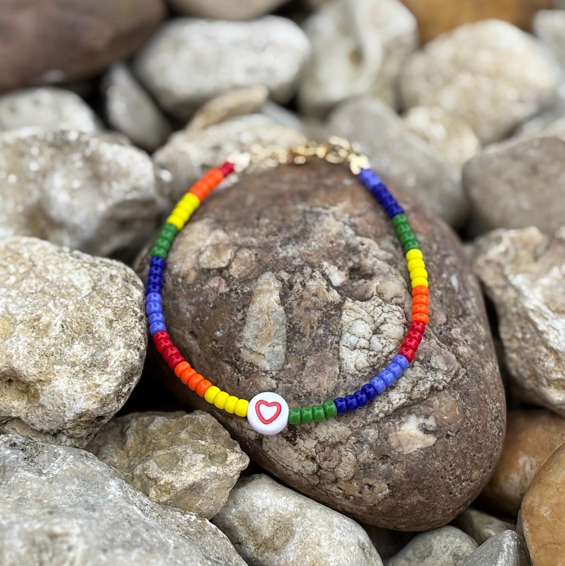 Colorful beaded bracelet with a heart charm on a rock surrounded by pebbles