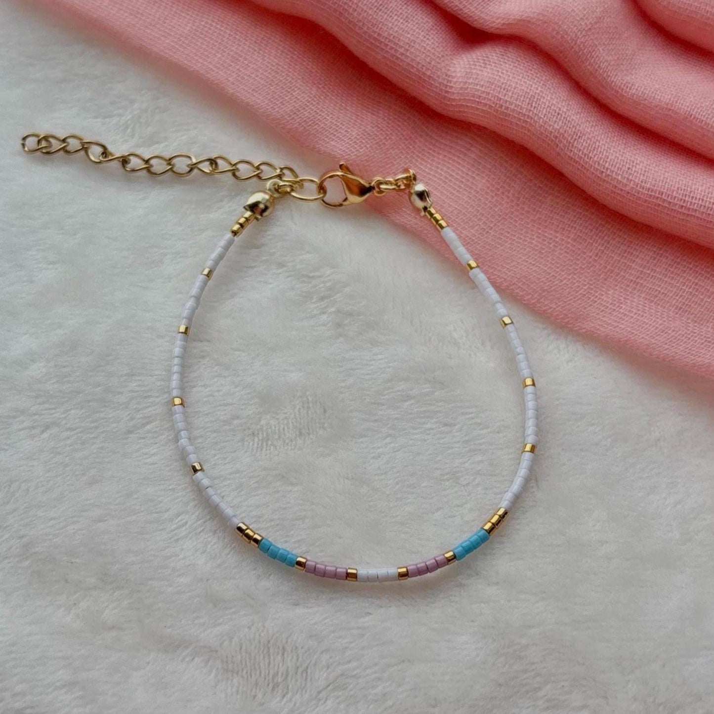 Bracelet with gold chain and colorful beads on a light pink fabric background