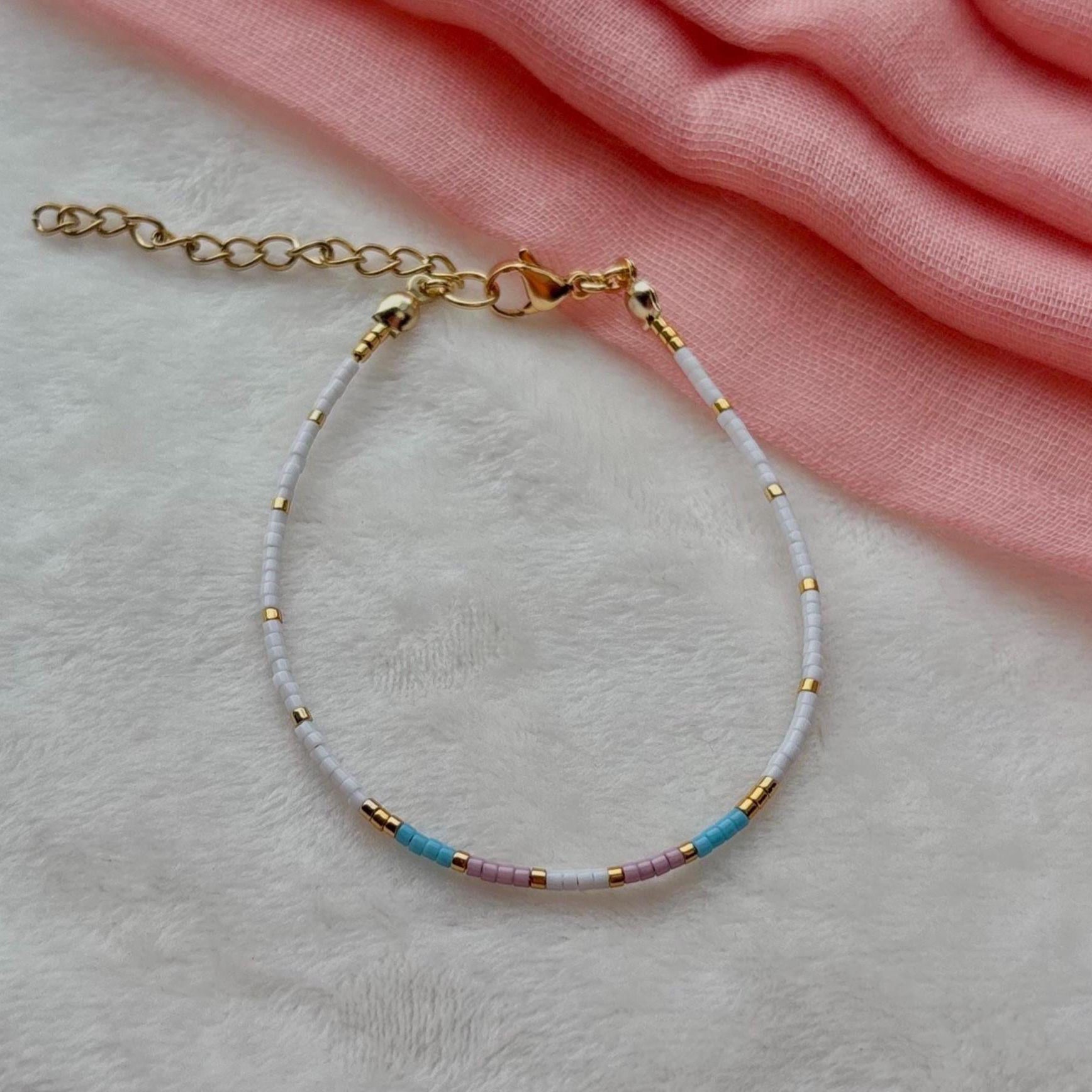 Bracelet with gold chain and colorful beads on a light pink fabric background