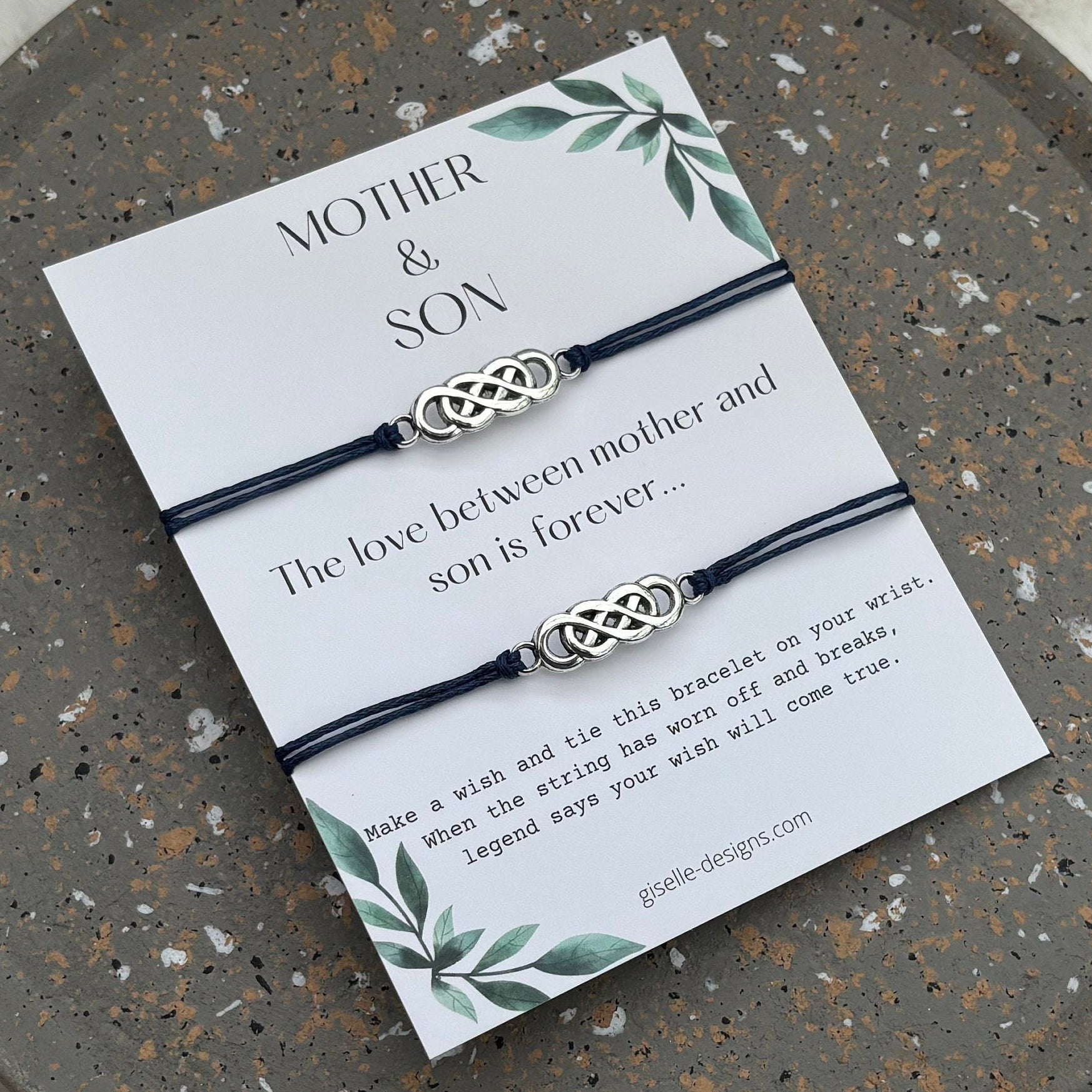 Two braided bracelets on a card with text and design elements, placed on a textured stone surface.