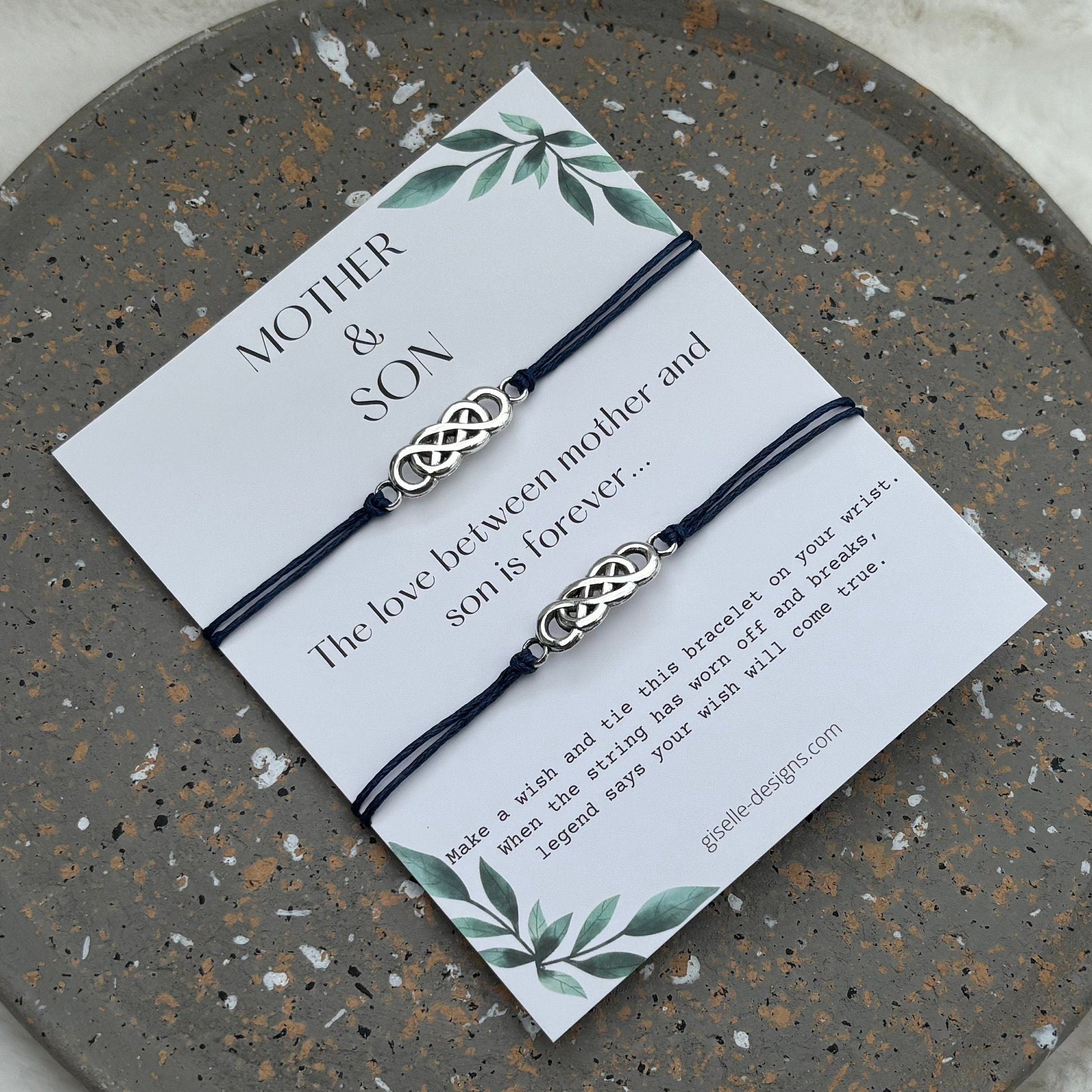 Two intertwined bracelets on a card with text and a decorative border, placed on a round stone surface.
