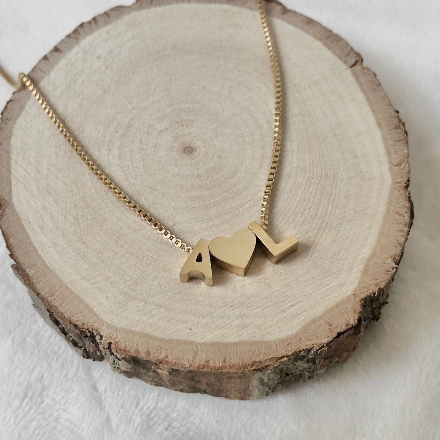 Gold necklace with 'AL' pendant on a wooden slice