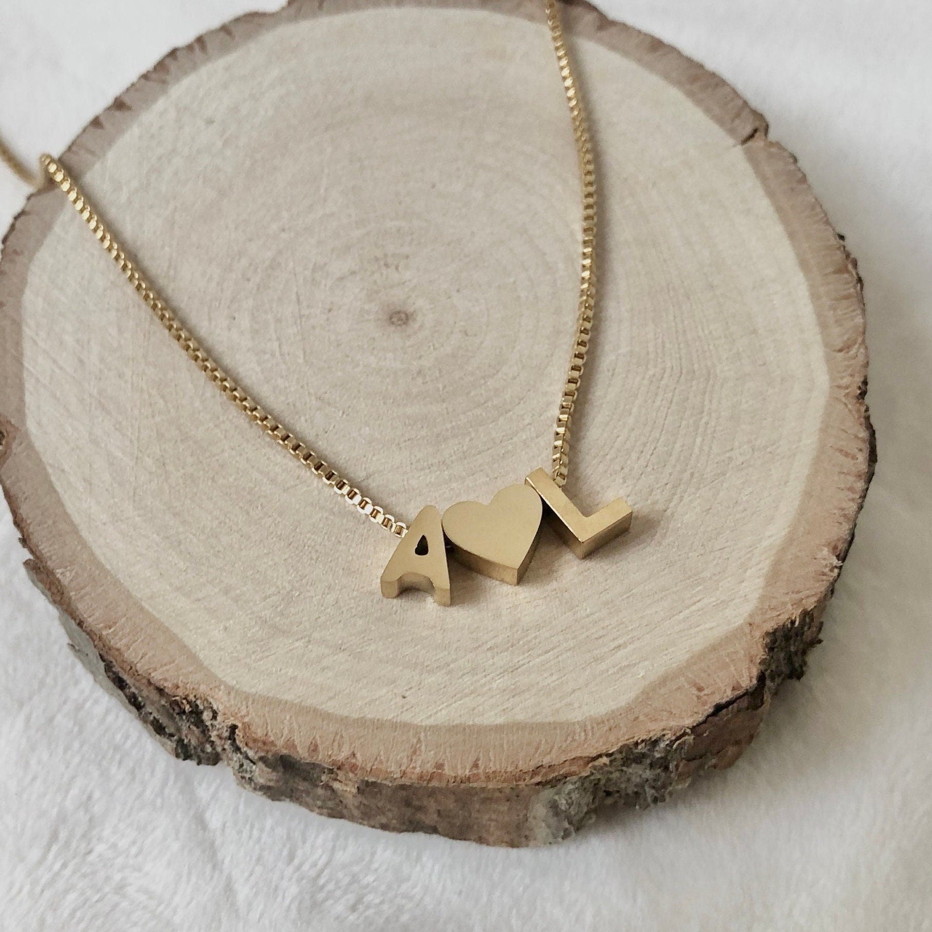 Gold necklace with 'AL' pendant on a wooden slice