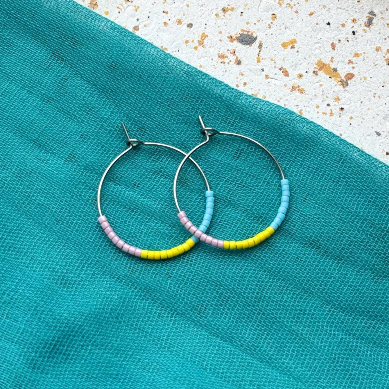 Hoop earrings with colorful beads on a teal fabric background