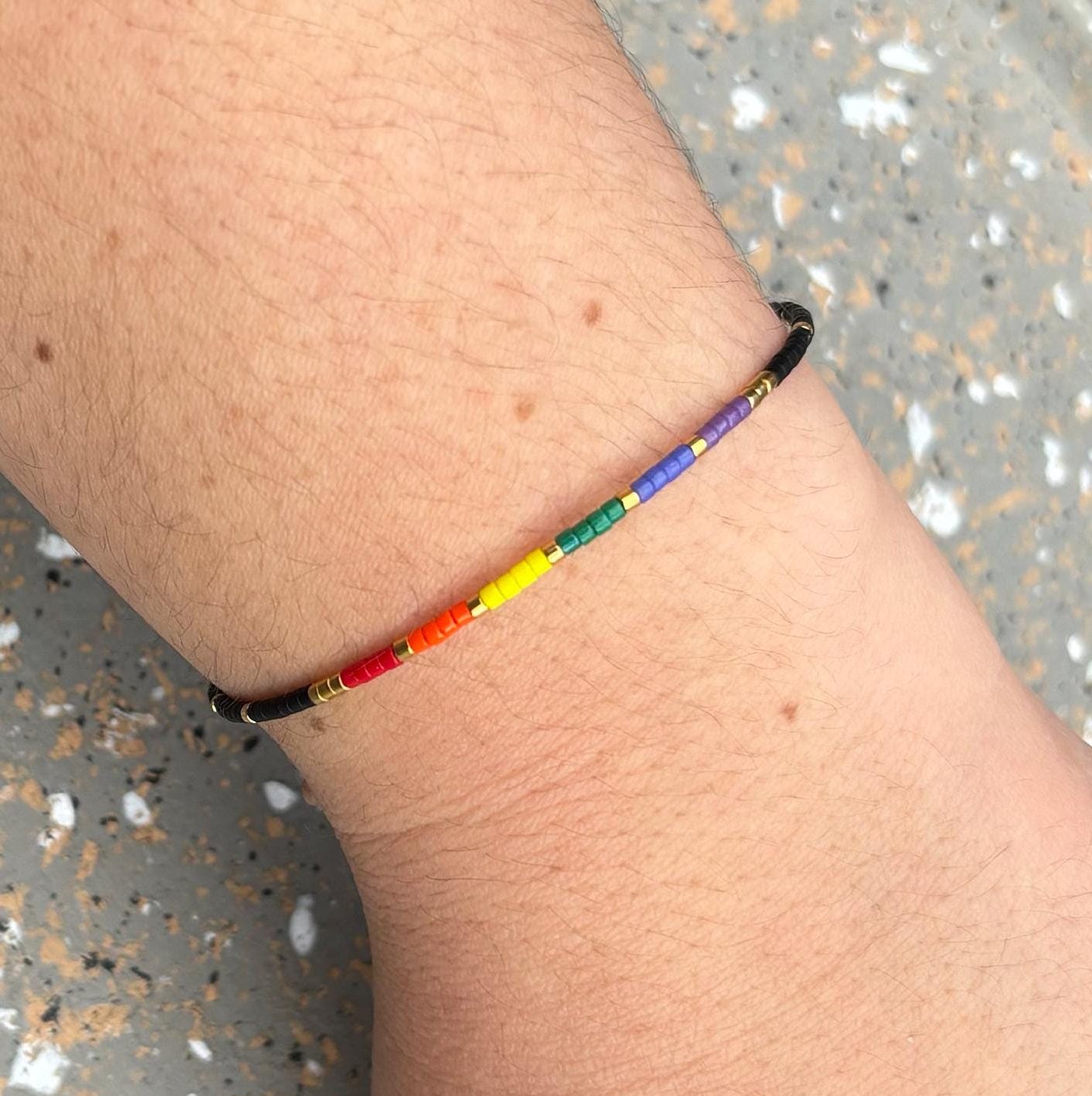 Rainbow beaded bracelet on a wrist with a speckled gray surface background