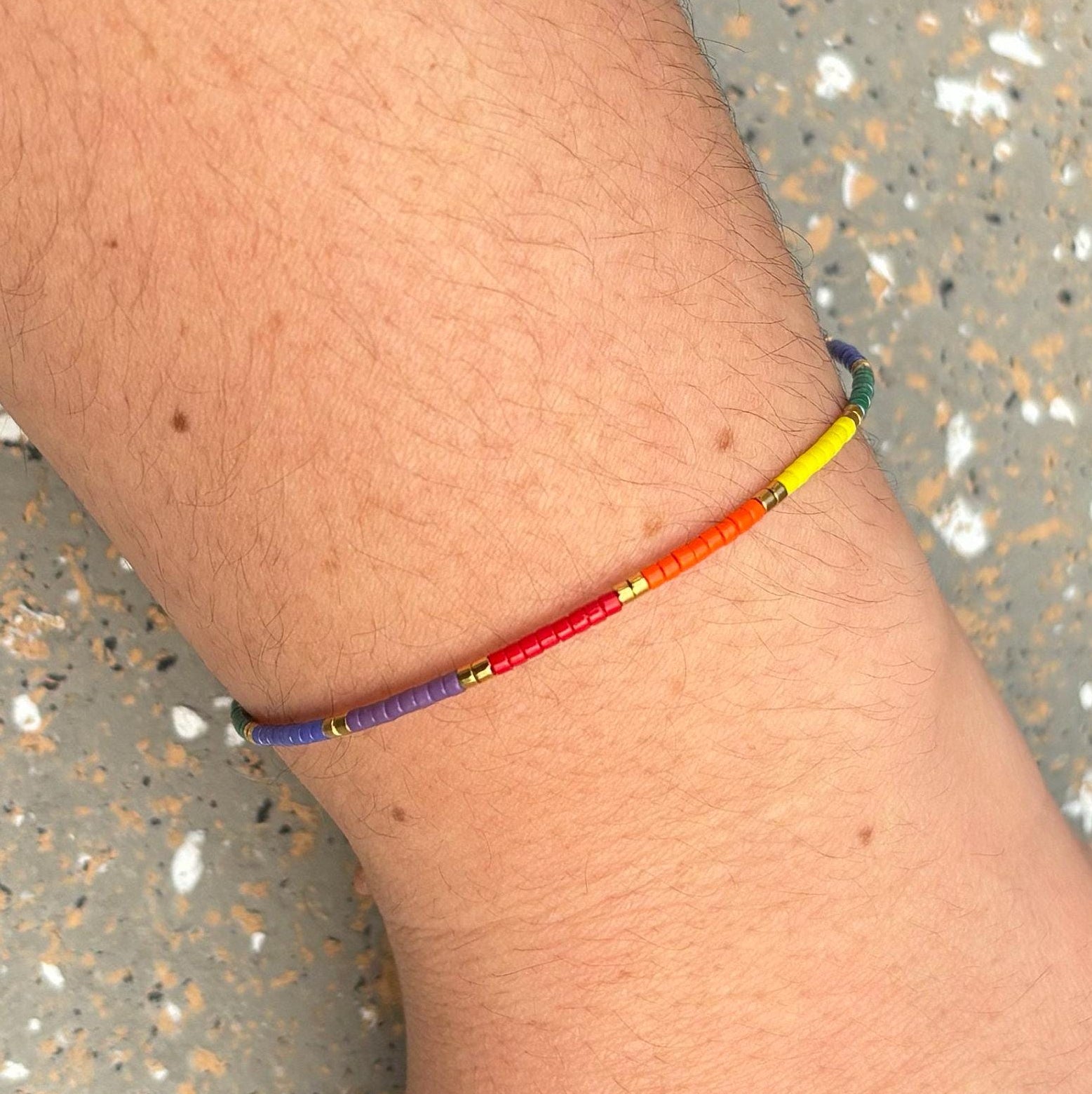 Multicolored beaded bracelet on a wrist with a speckled surface background