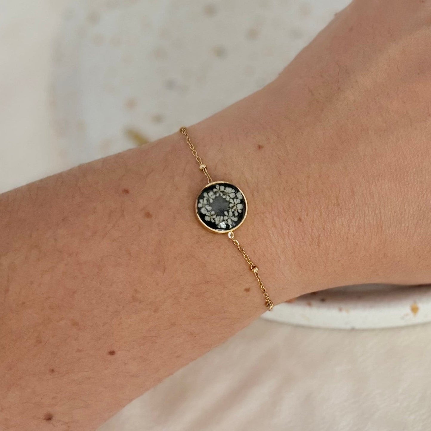 Gold bracelet with a dark gemstone on a wrist against a neutral background