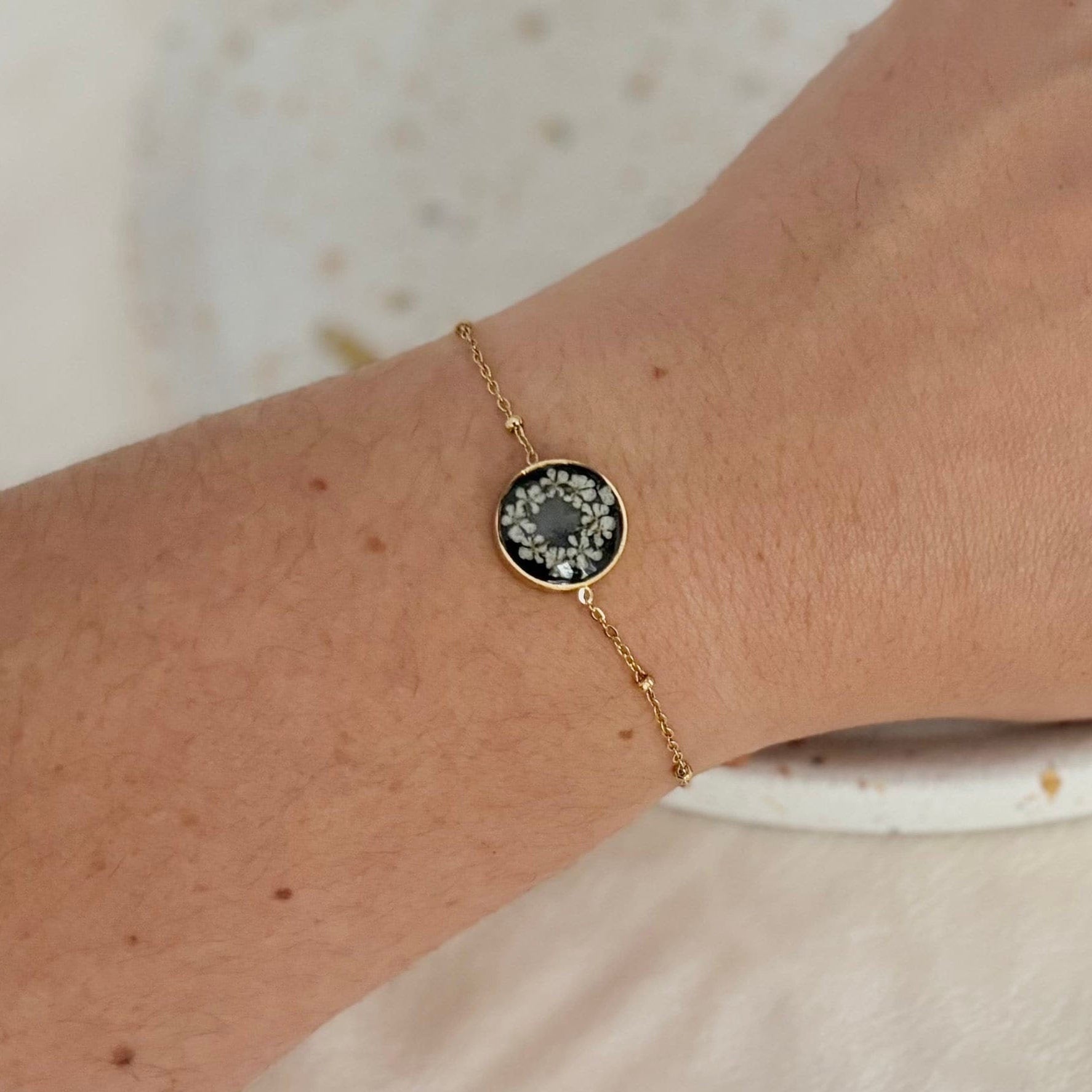 Gold bracelet with a dark gemstone on a wrist against a neutral background