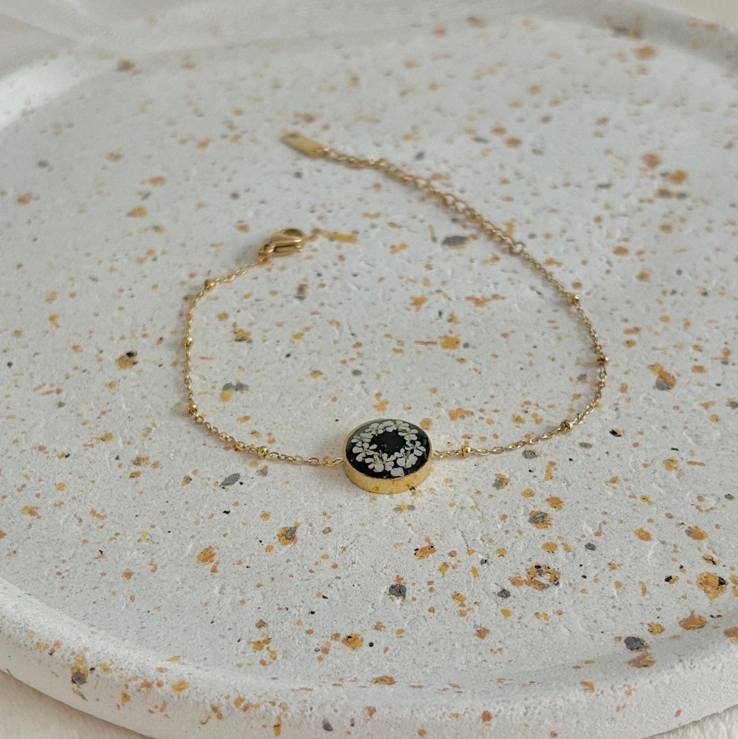 Gold bracelet with a black stone on a speckled ceramic surface