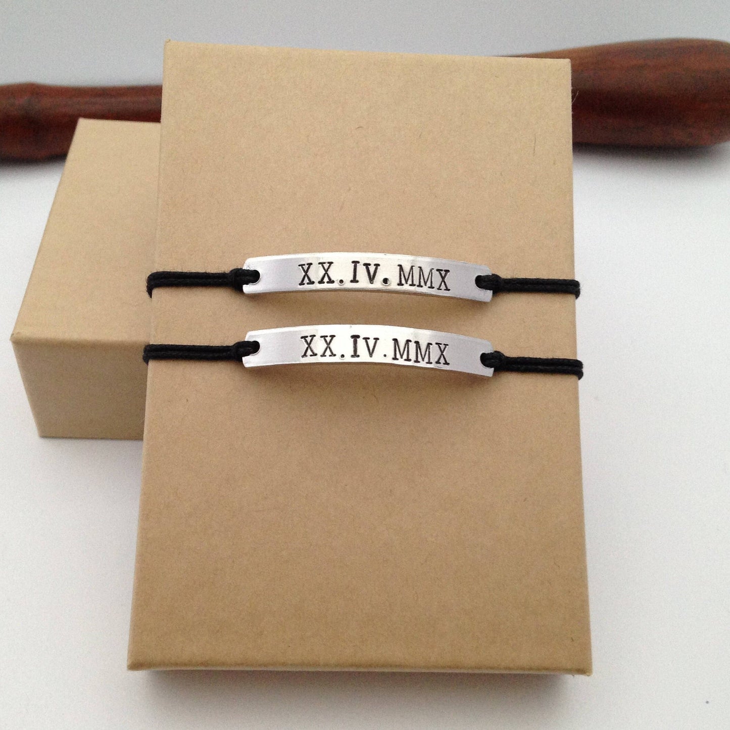 Two silver bracelets with black strings on a brown box