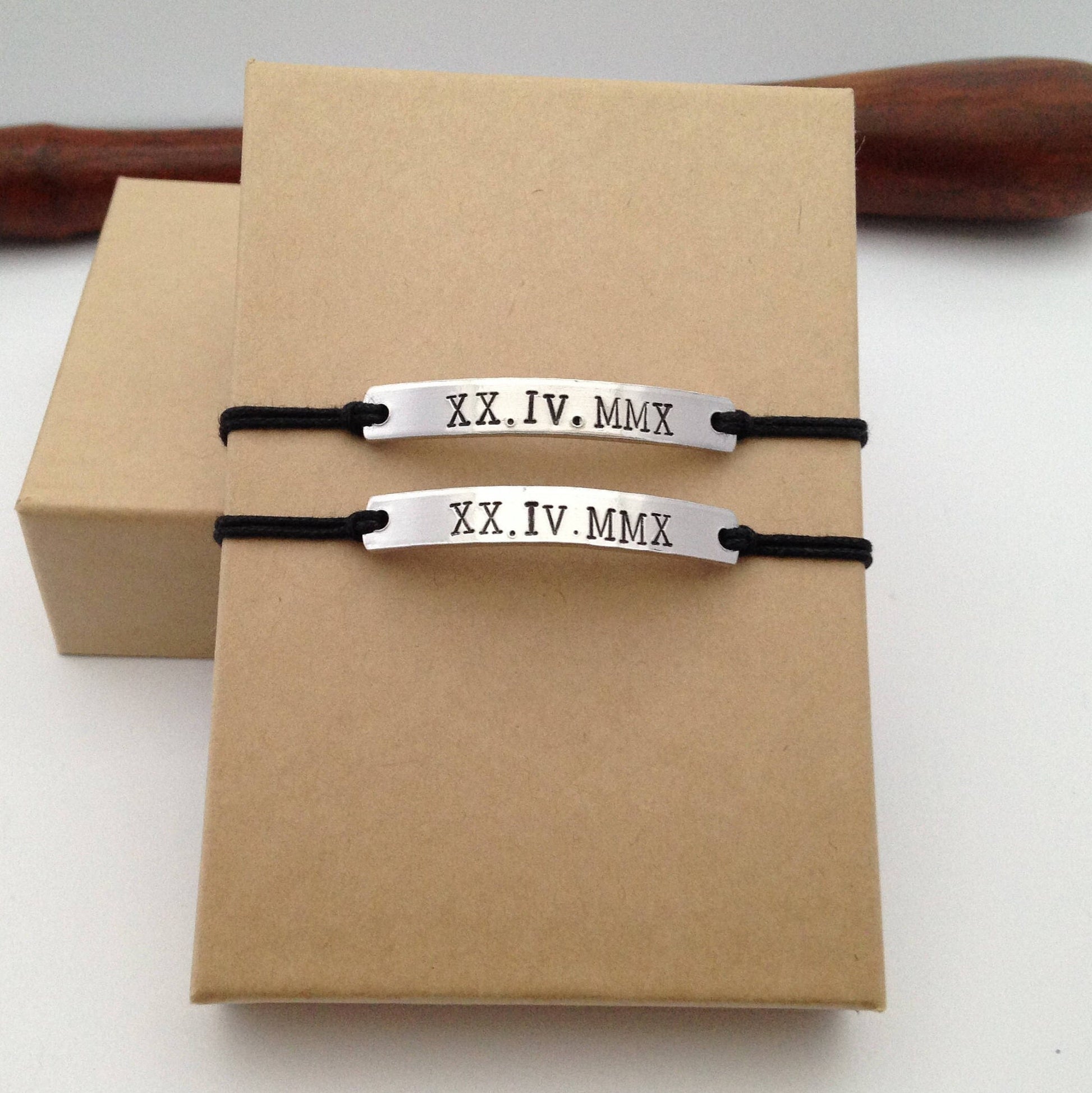 Two silver bracelets with black strings on a brown box