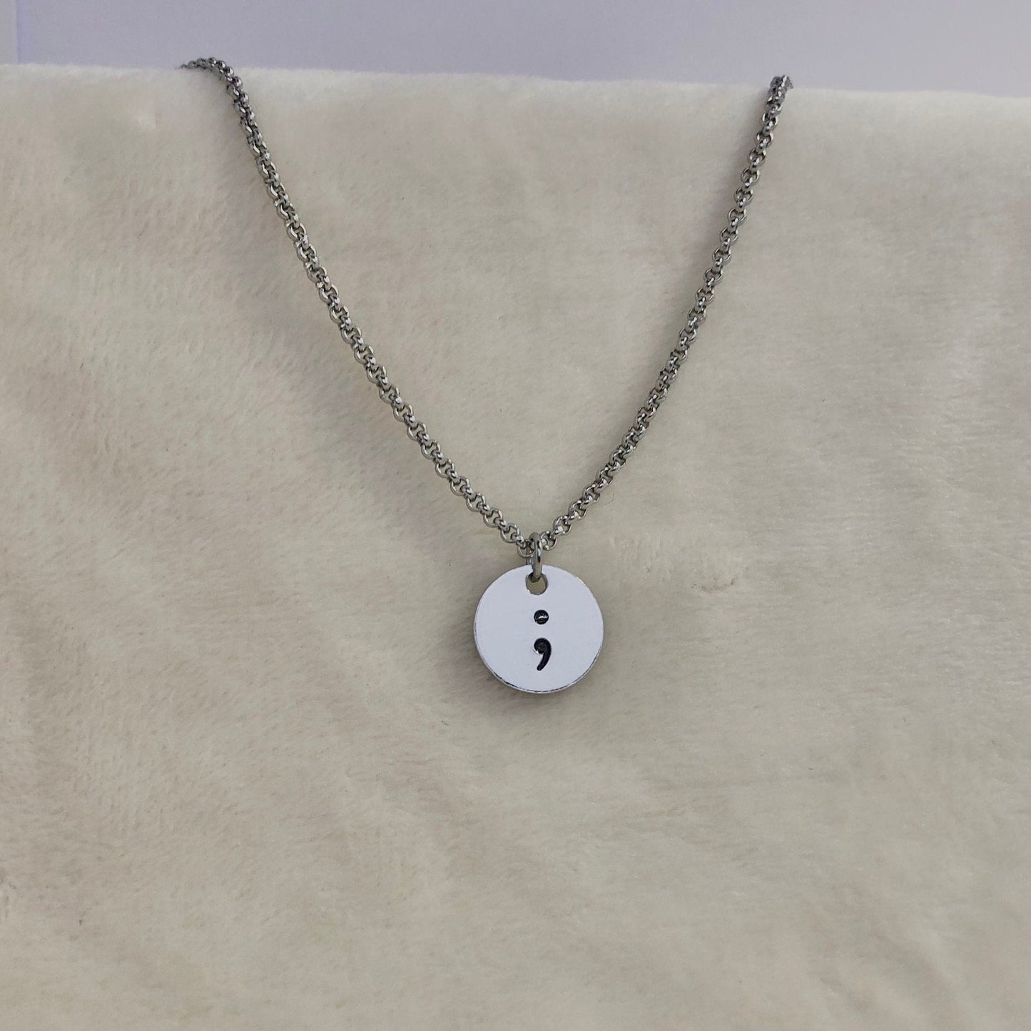 Necklace with a round pendant featuring a semicolon on a beige surface