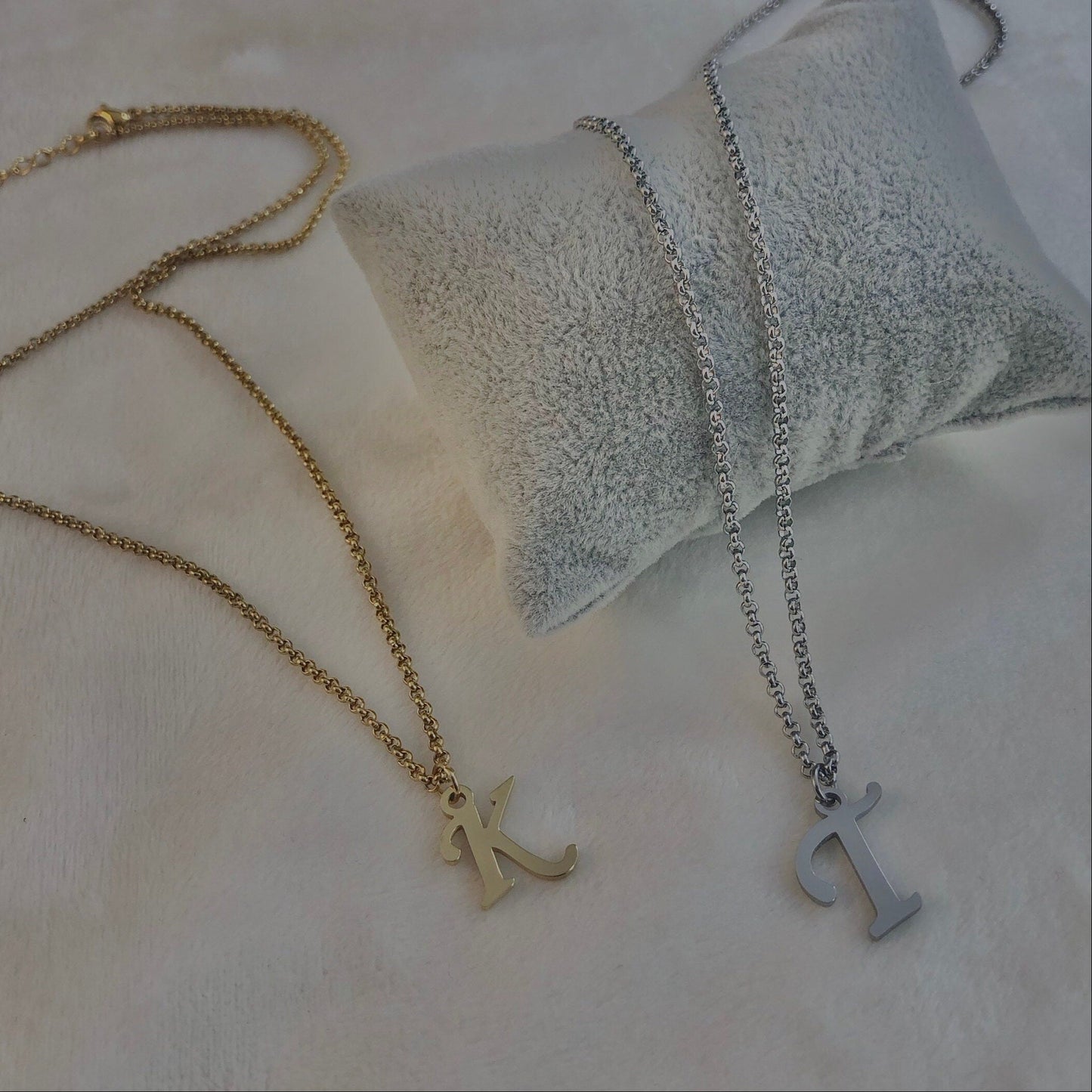 Two necklaces, one gold and one silver, on a textured surface.