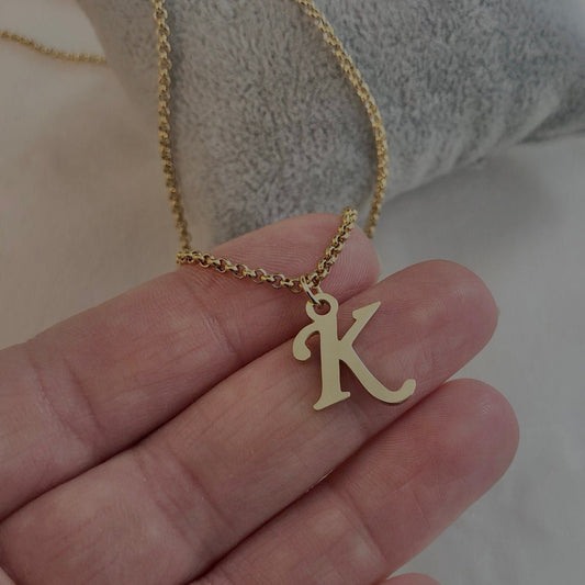 Gold necklace with a 'K' pendant held in a hand against a neutral background