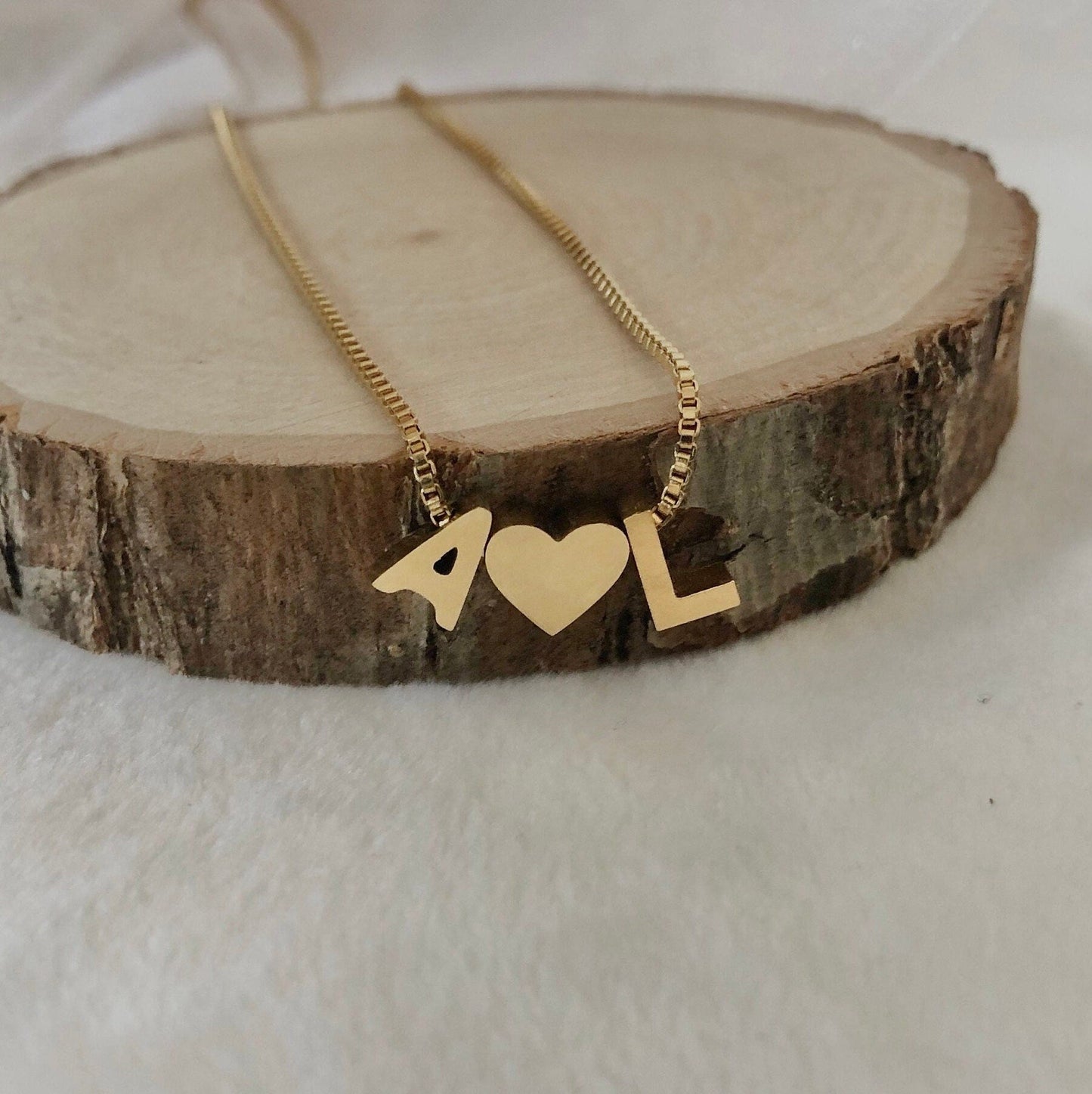Gold necklace with heart and '4L' pendant on a wooden block