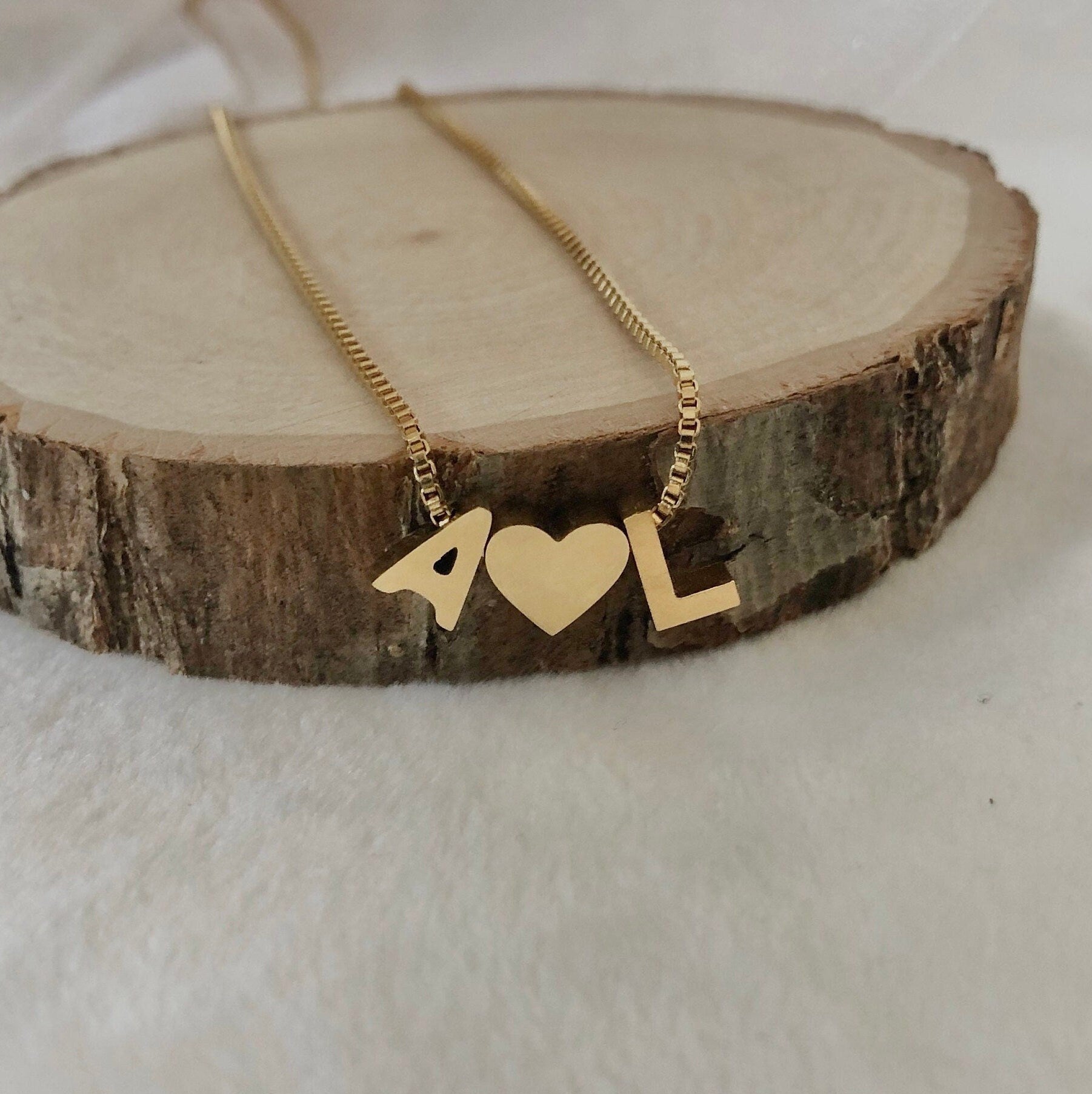Gold necklace with heart and '4L' pendant on a wooden block