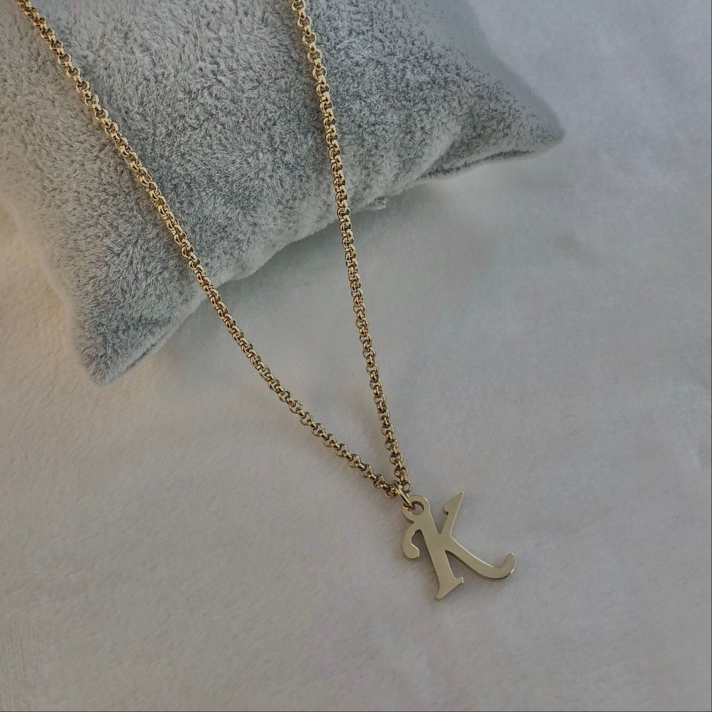 Gold necklace with a 'K' pendant on a textured surface