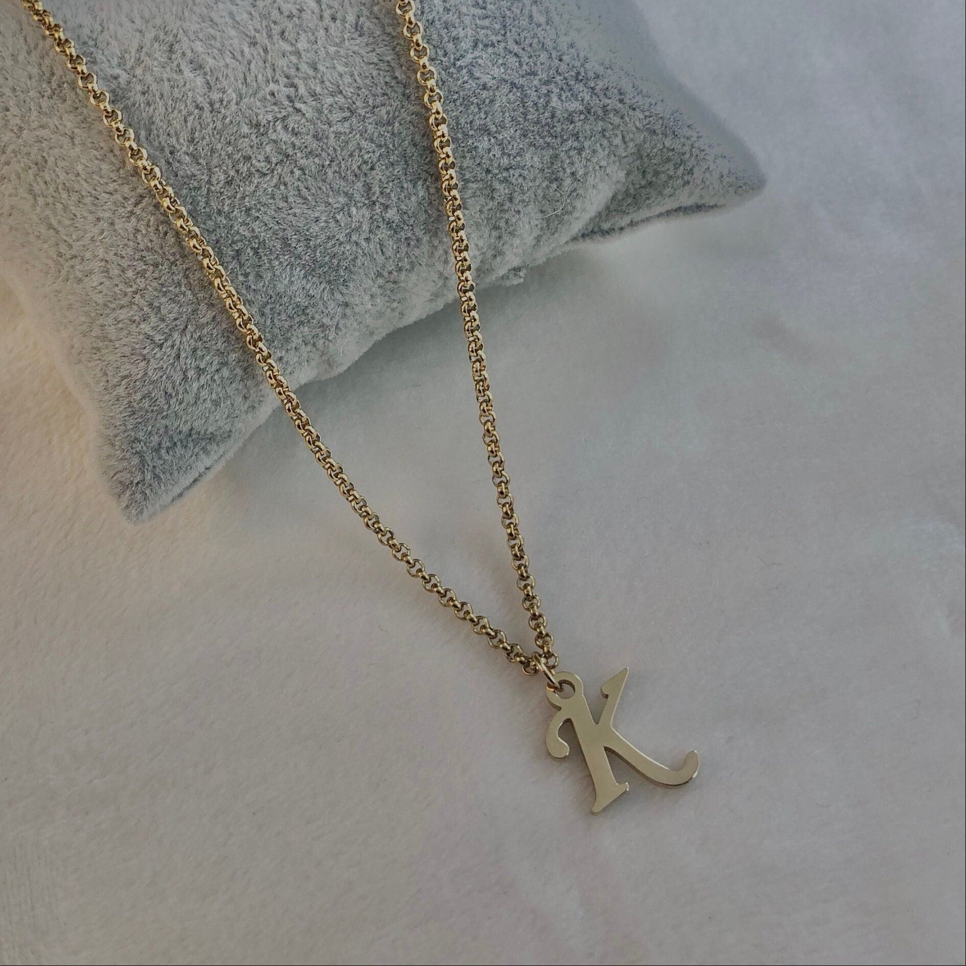 Gold necklace with a 'K' pendant on a textured surface