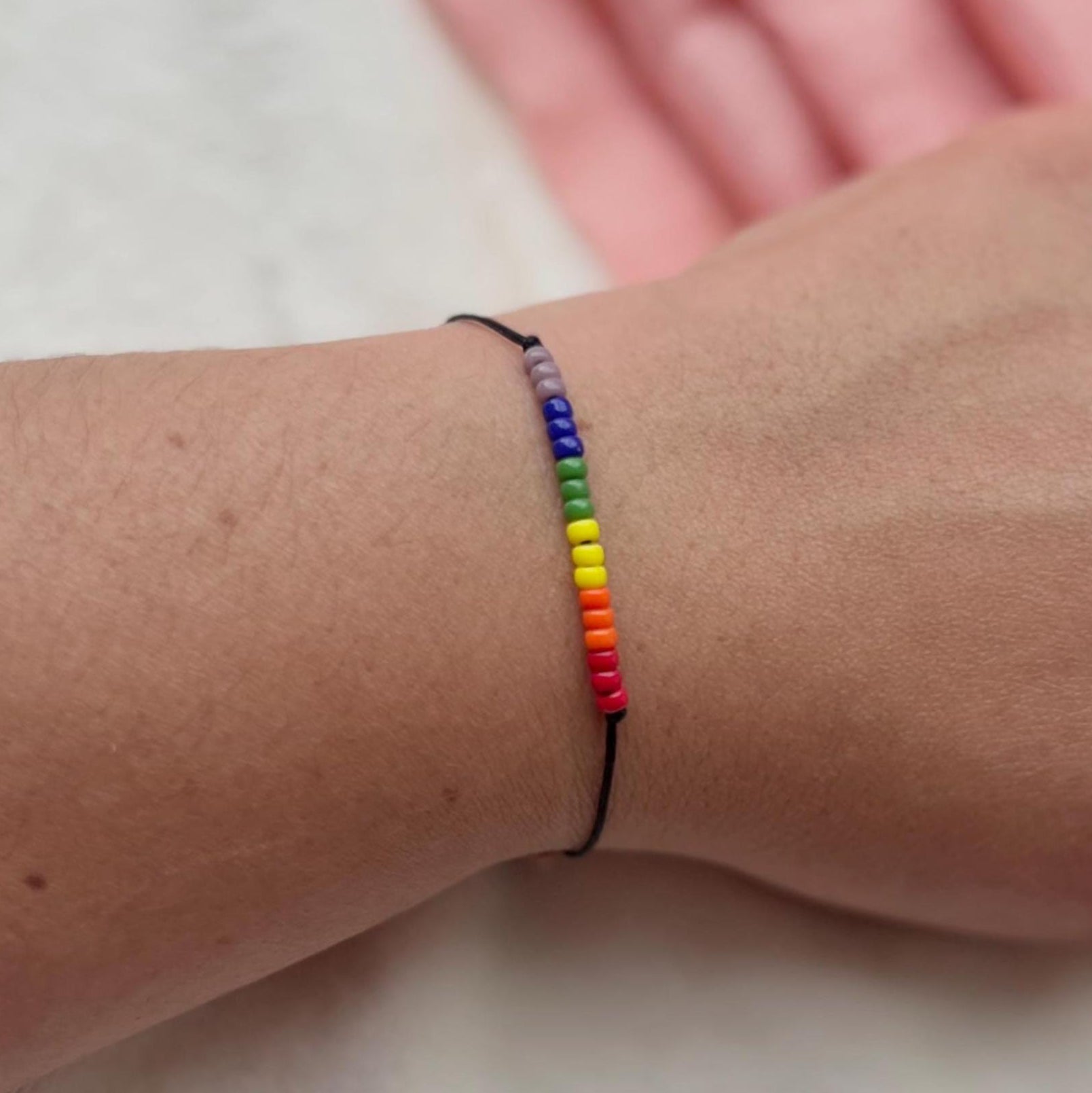 Rainbow bracelet on a wrist with a white and pink background